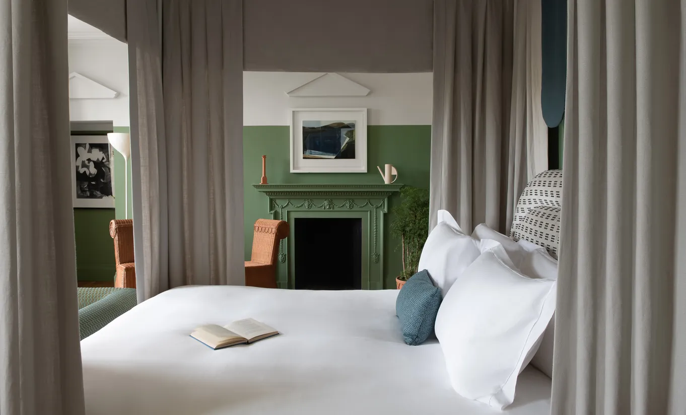 Chambre avec grand lit blanc, murs verts, cheminée et rideaux au sol dans la Cowley Manor Suite de Cowley Manor Experimental, retraite à la campagne dans les Cotswolds