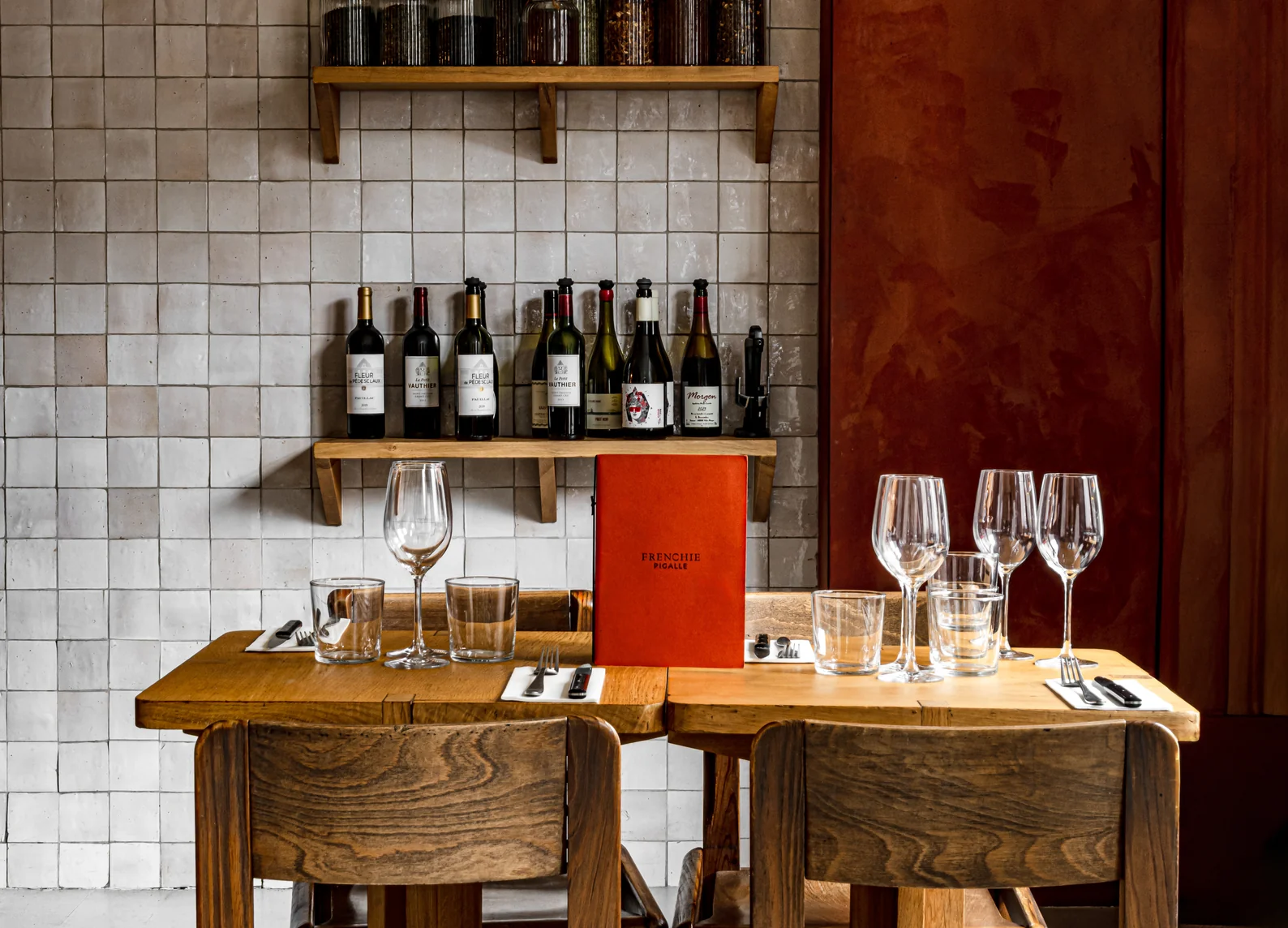 Mesa de madera con el menú rojo de Frenchie Pigalle, copas de vino y estantes para botellas de vino en el restaurante Frenchie Pigalle, Grand Pigalle Experimental, París 9