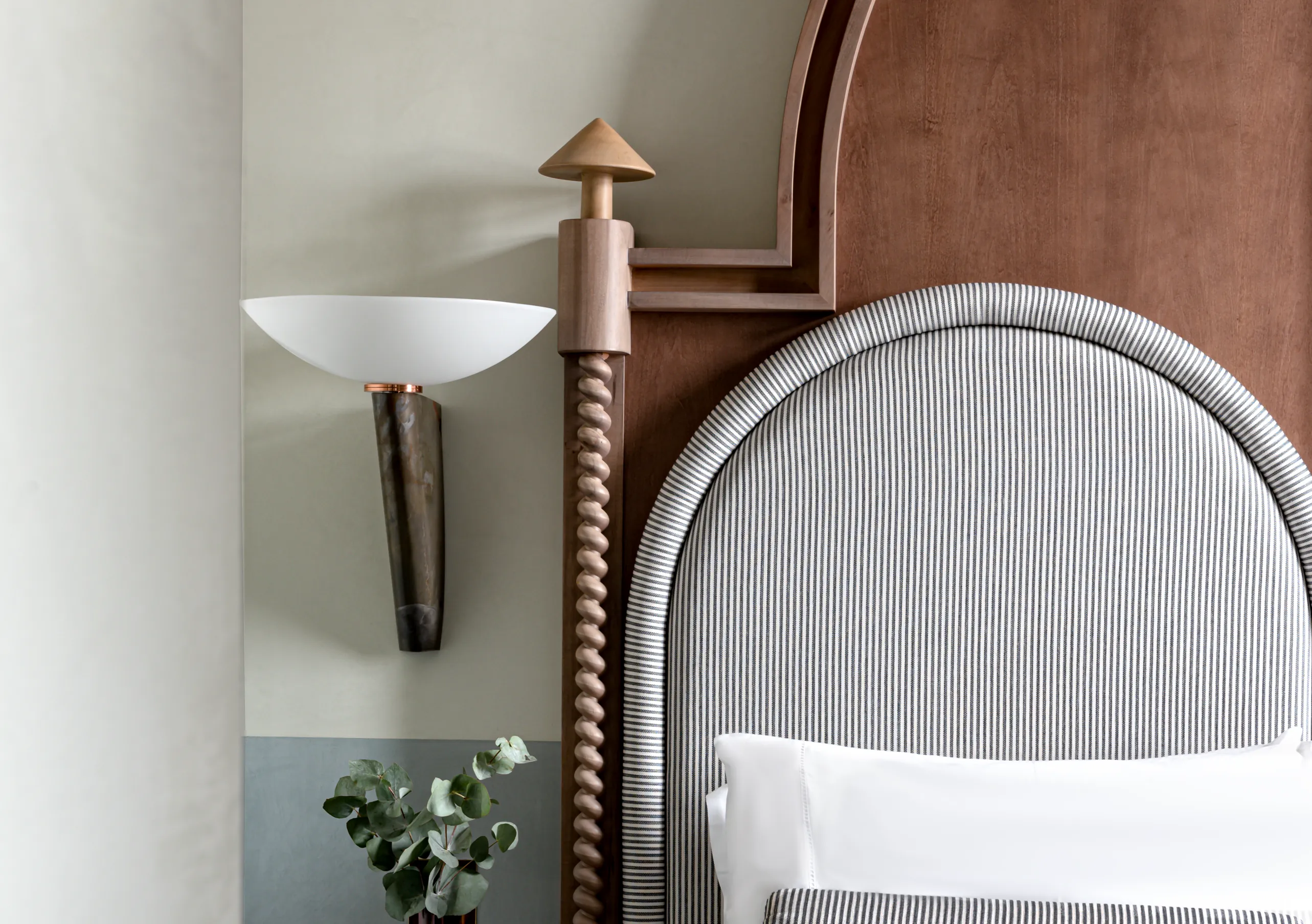 Il Palazzo Experimental close-up of a striped arched headboard with twisted wood bedpost and sculptural brass wall sconce in Venice