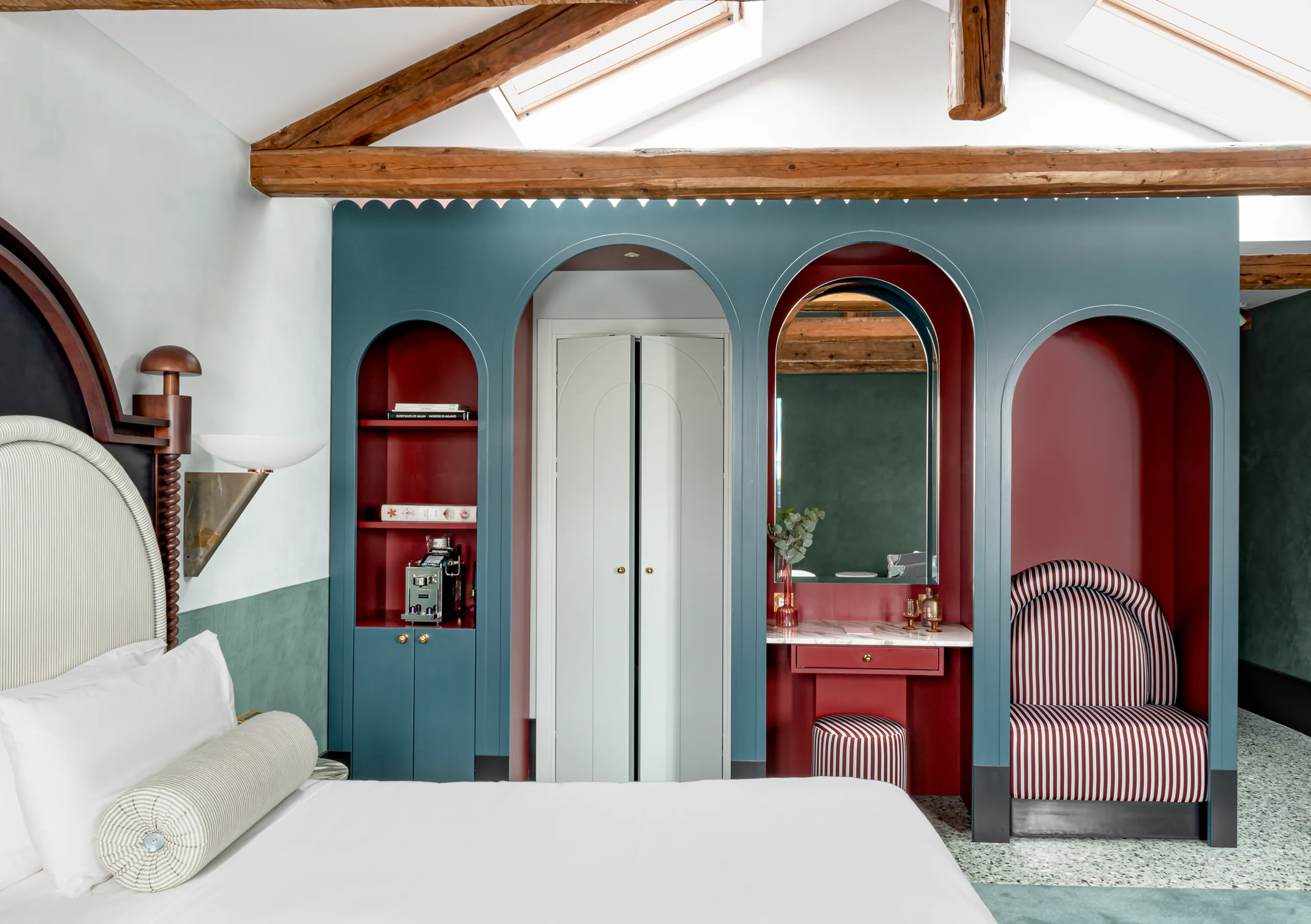 Il Palazzo Experimental suite with blue and red arched alcoves, skylight, dressing table and striped armchair in Venice.