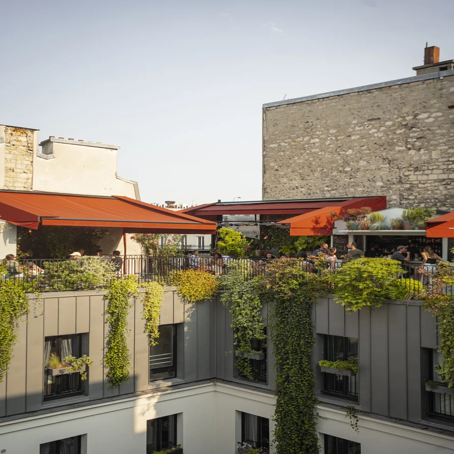 Lively green rooftop terrace with red awnings and guests in summer at Grands Boulevards Experimental, Paris 2