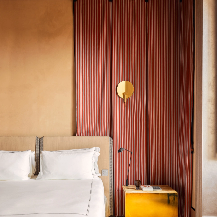 Bedroom with white bed, beige headboard and red striped wallpaper with golden wall light at Experimental Roma, Rome