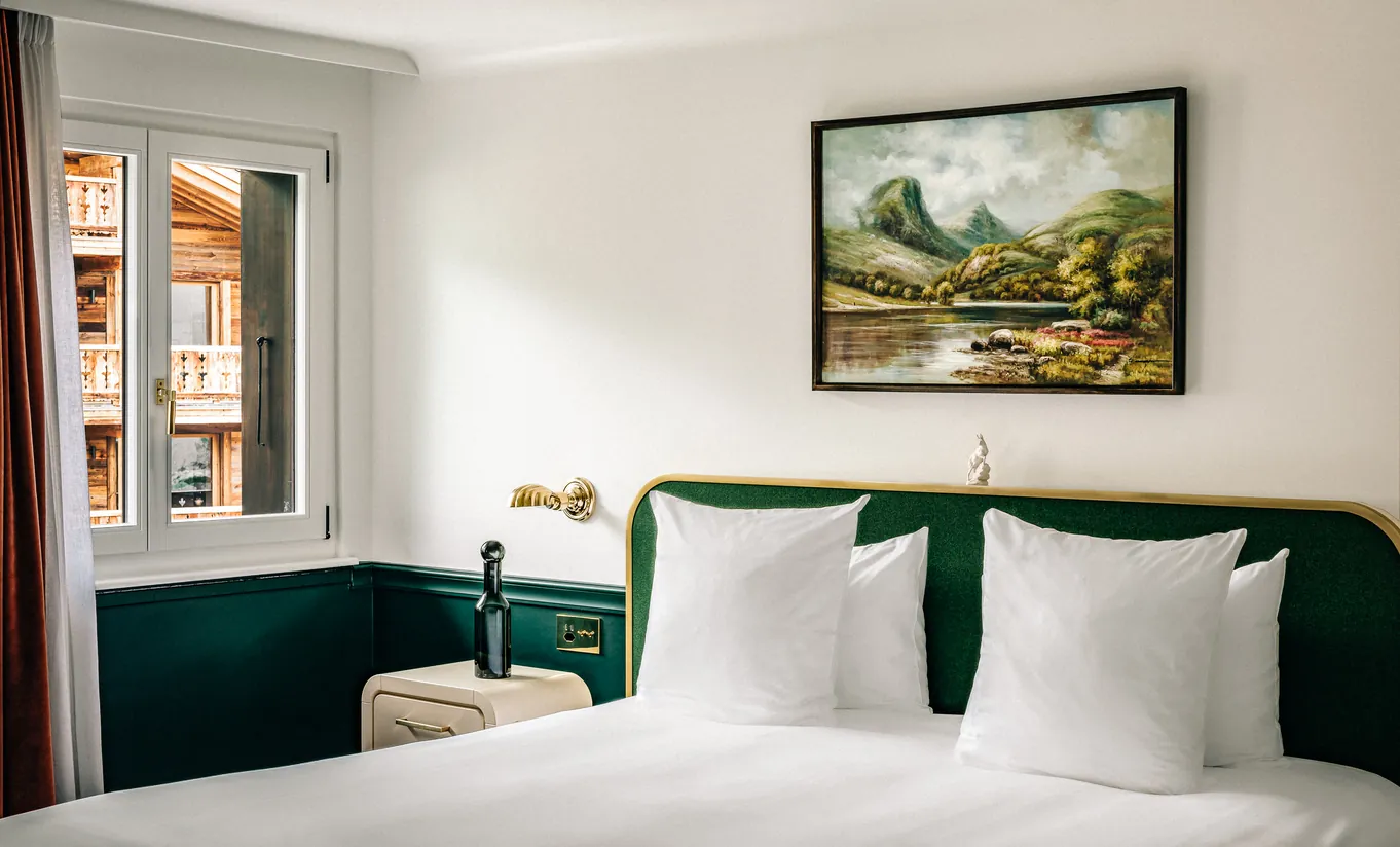 Bright bedroom with a white double bed, green headboard and a landscape painting on the wall in the Classic Room at Experimental Chalet Verbier