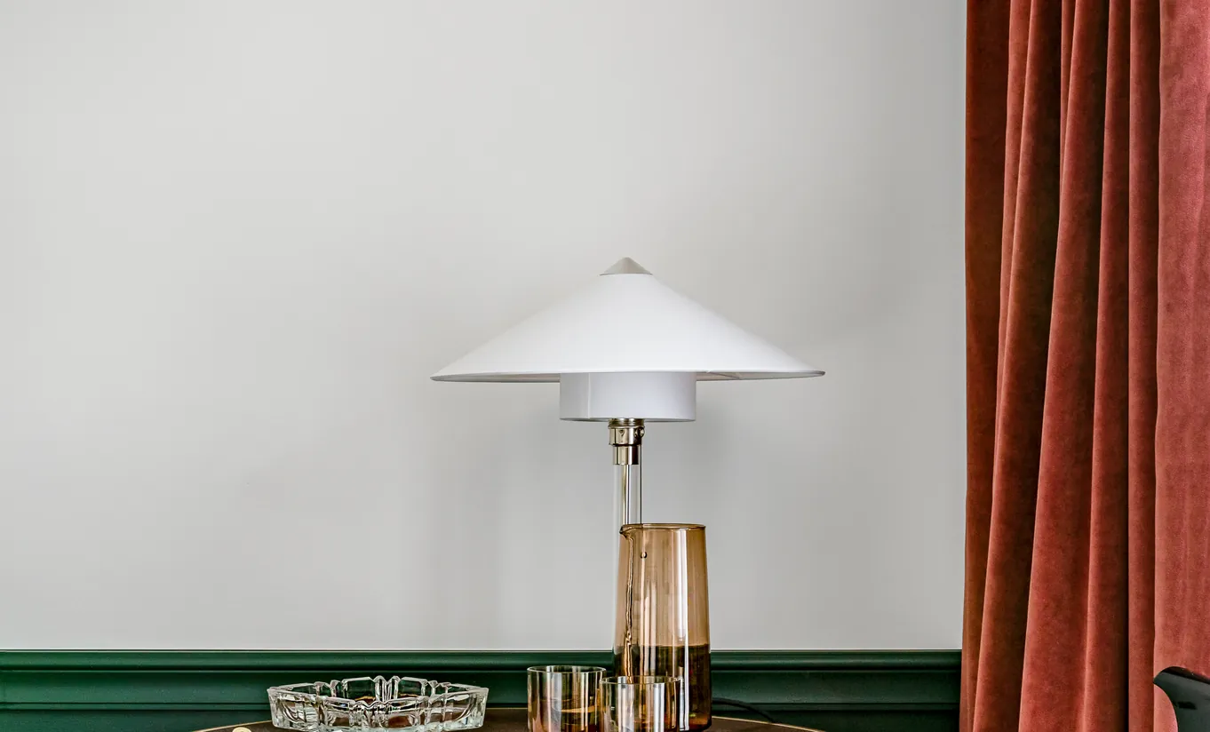 Bedside area with a brass lamp and wooden side table against green panelling and red curtains in the Classic Room at Experimental Chalet Verbier
