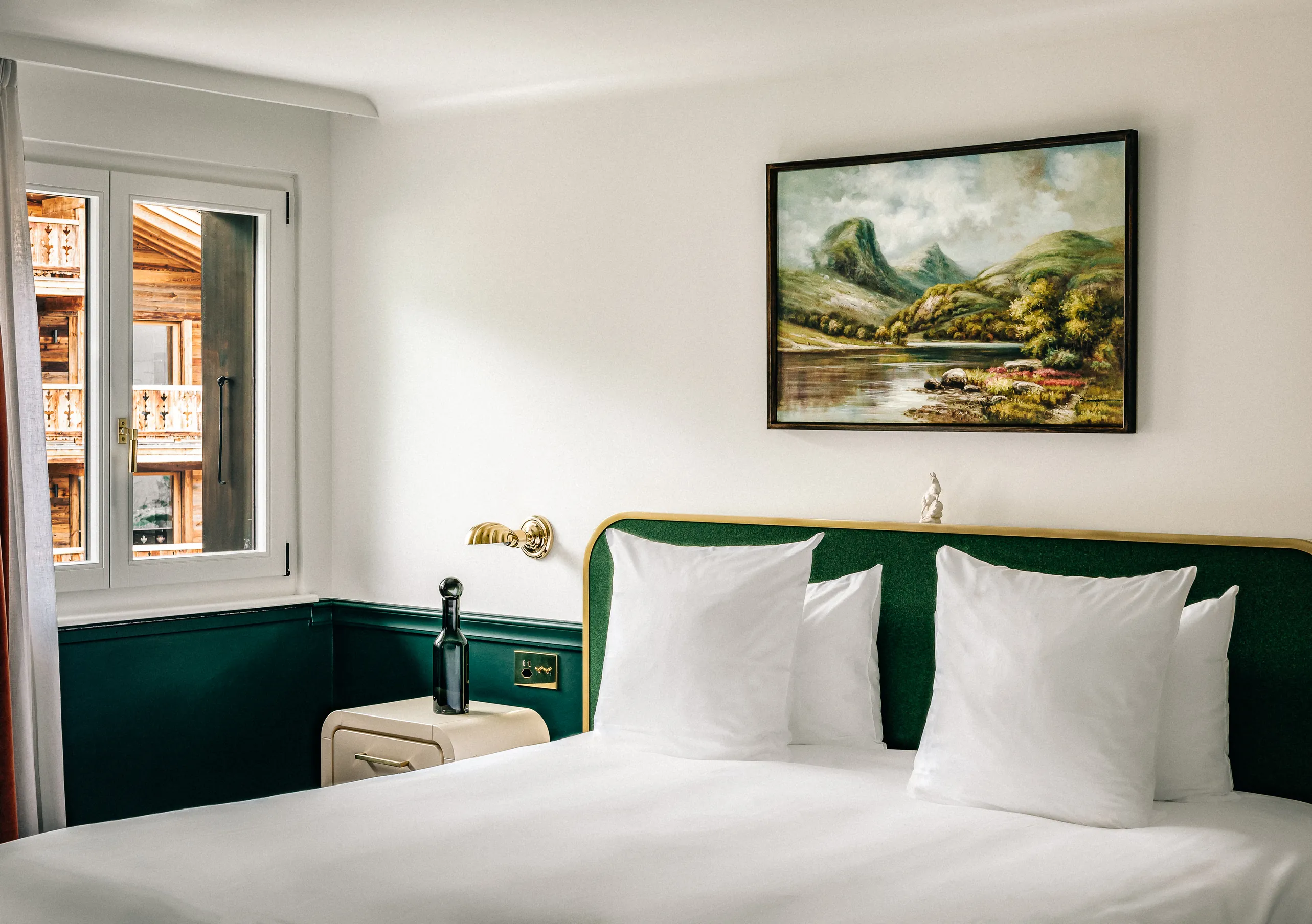 Bright bedroom with a white double bed, green headboard and a landscape painting on the wall in the Classic Room at Experimental Chalet Verbier