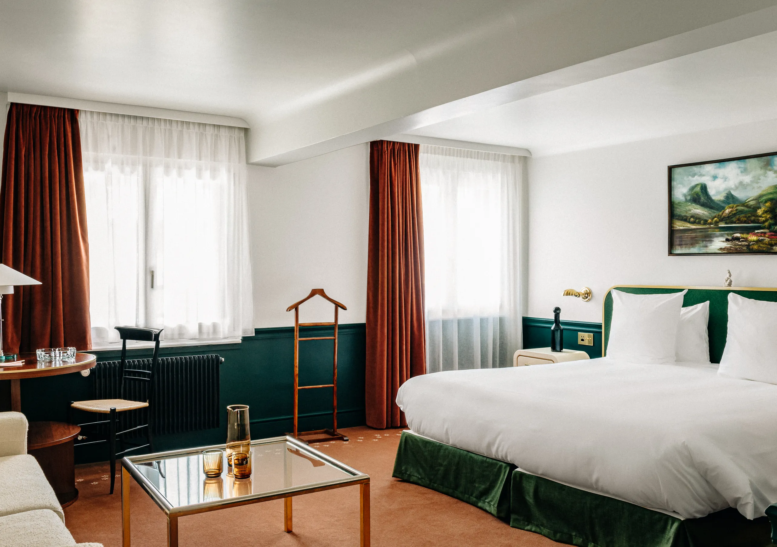 Bright bedroom with a white double bed, green armchair and red curtains in the Junior Suite at Experimental Chalet Verbier