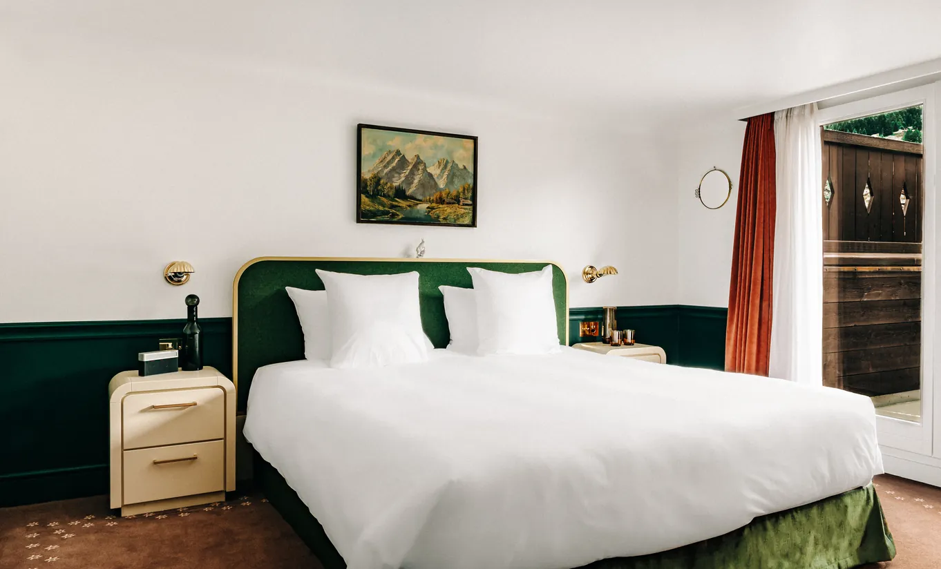 Bright bedroom with a white king-size bed, dark green headboard and red curtains in the Verbier Suite at Experimental Chalet Verbier
