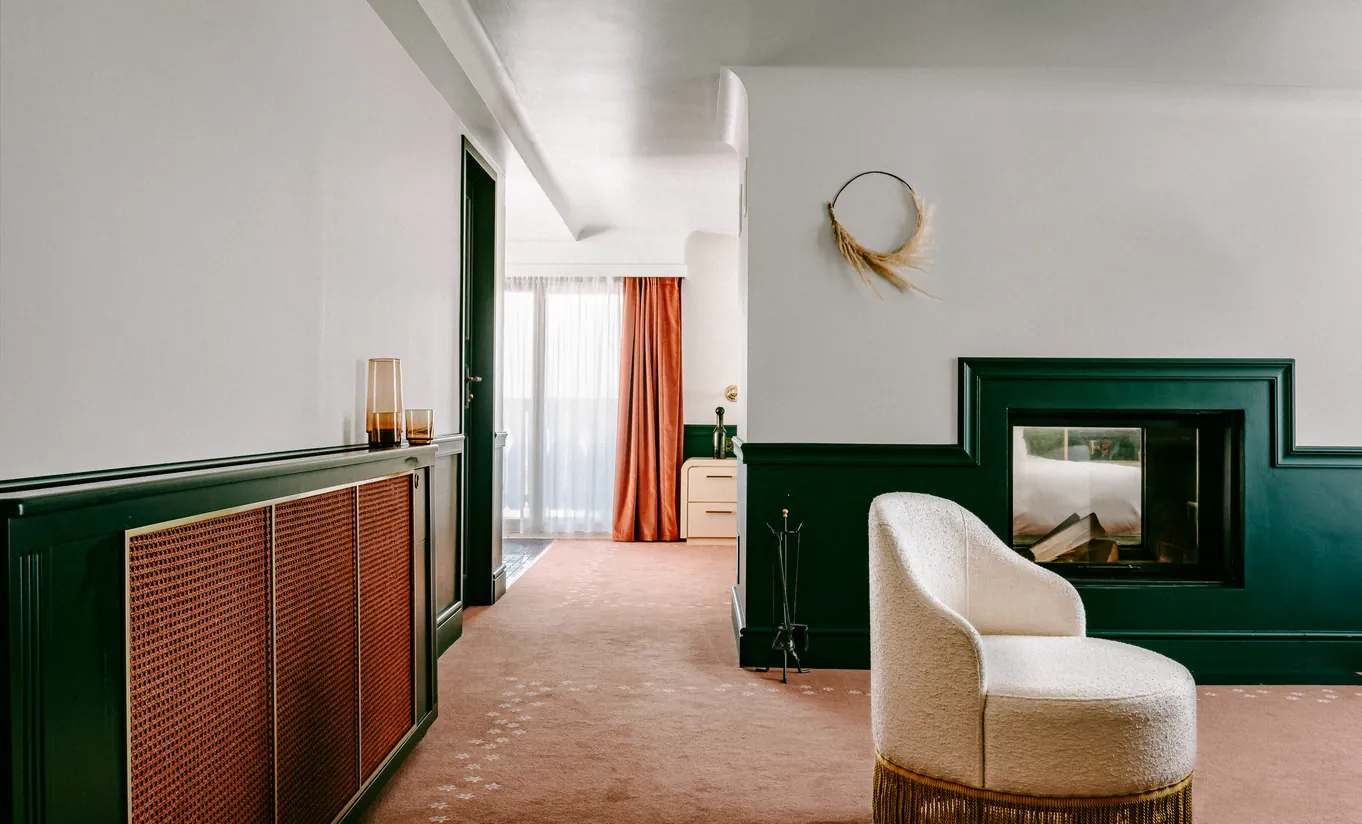 Bright room with a dark green fireplace and white armchair in the Panorama Suite at Experimental Chalet Verbier