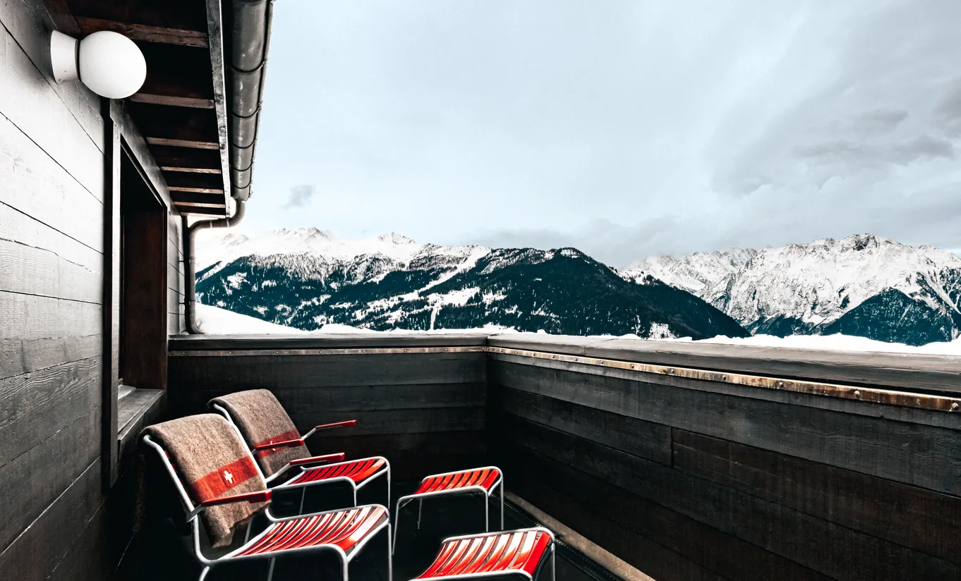 Private terrace with red chairs and a panoramic view of the snowy Swiss Alps in the Panorama Suite at Experimental Chalet Verbier