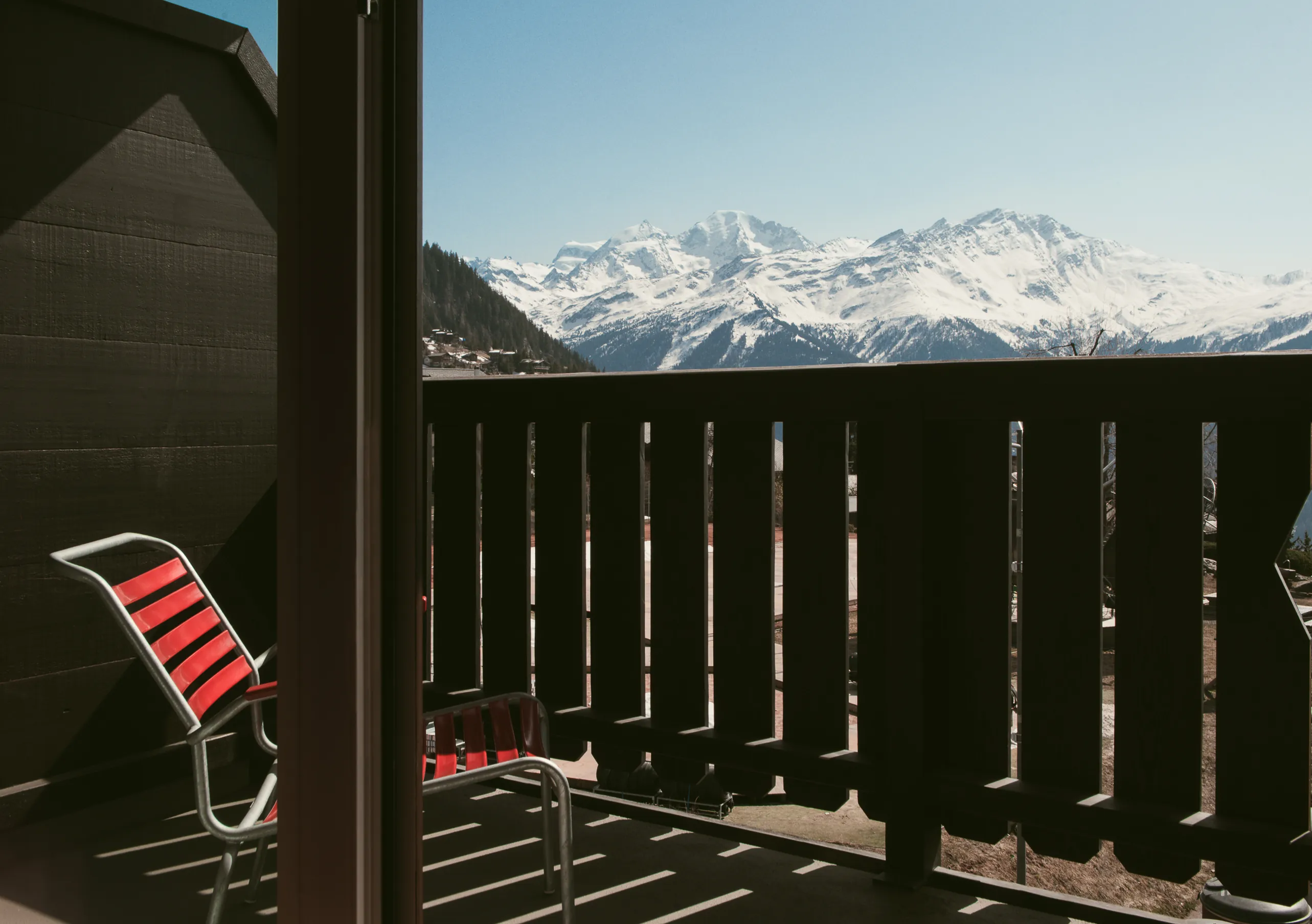 Private terrace with a red chair and a panoramic view of the snowy Swiss Alps in the Deluxe Room Terrace at Experimental Chalet Verbier