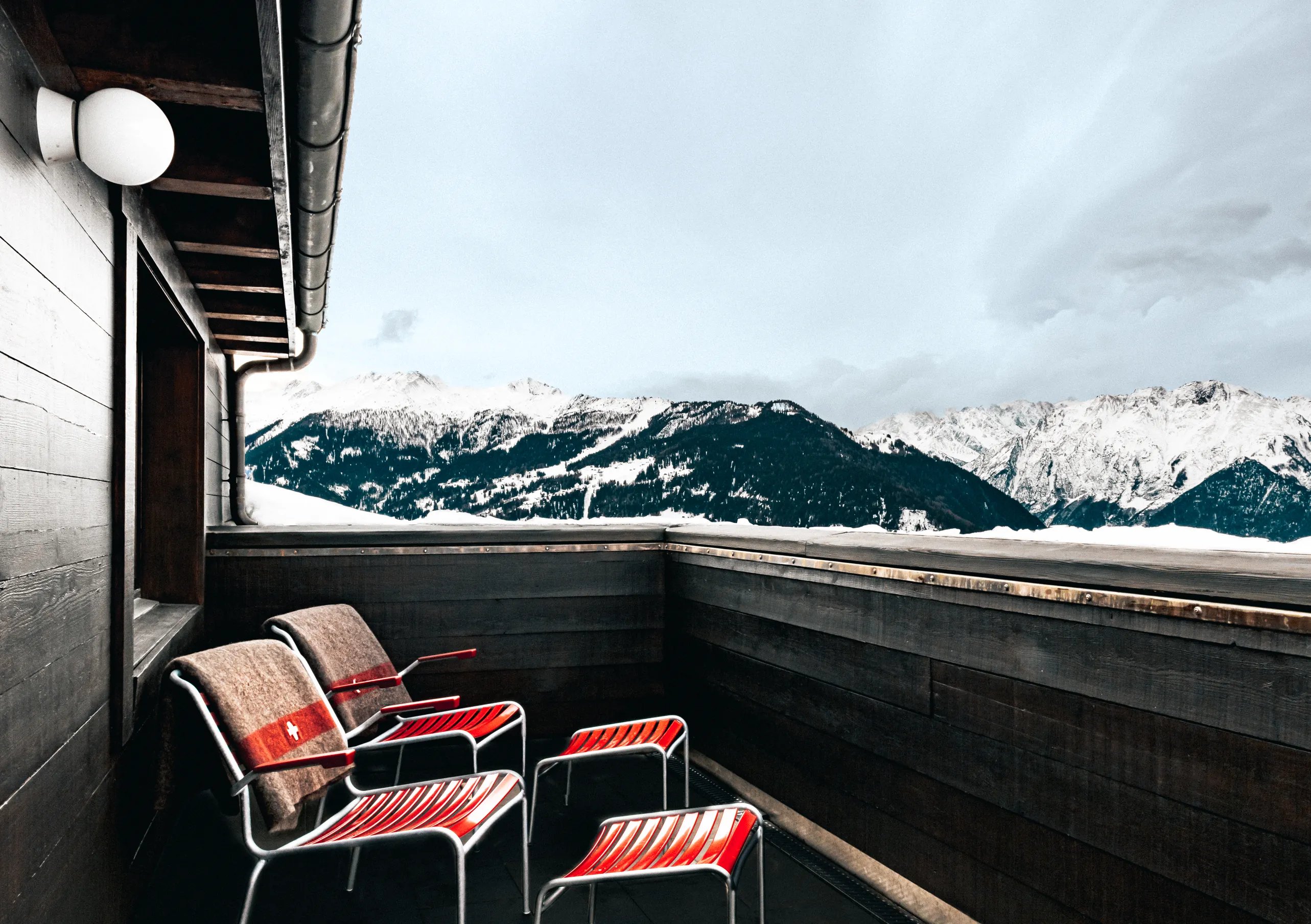 Private terrace with red chairs and a panoramic view of the snowy Swiss Alps in the Panorama Suite at Experimental Chalet Verbier