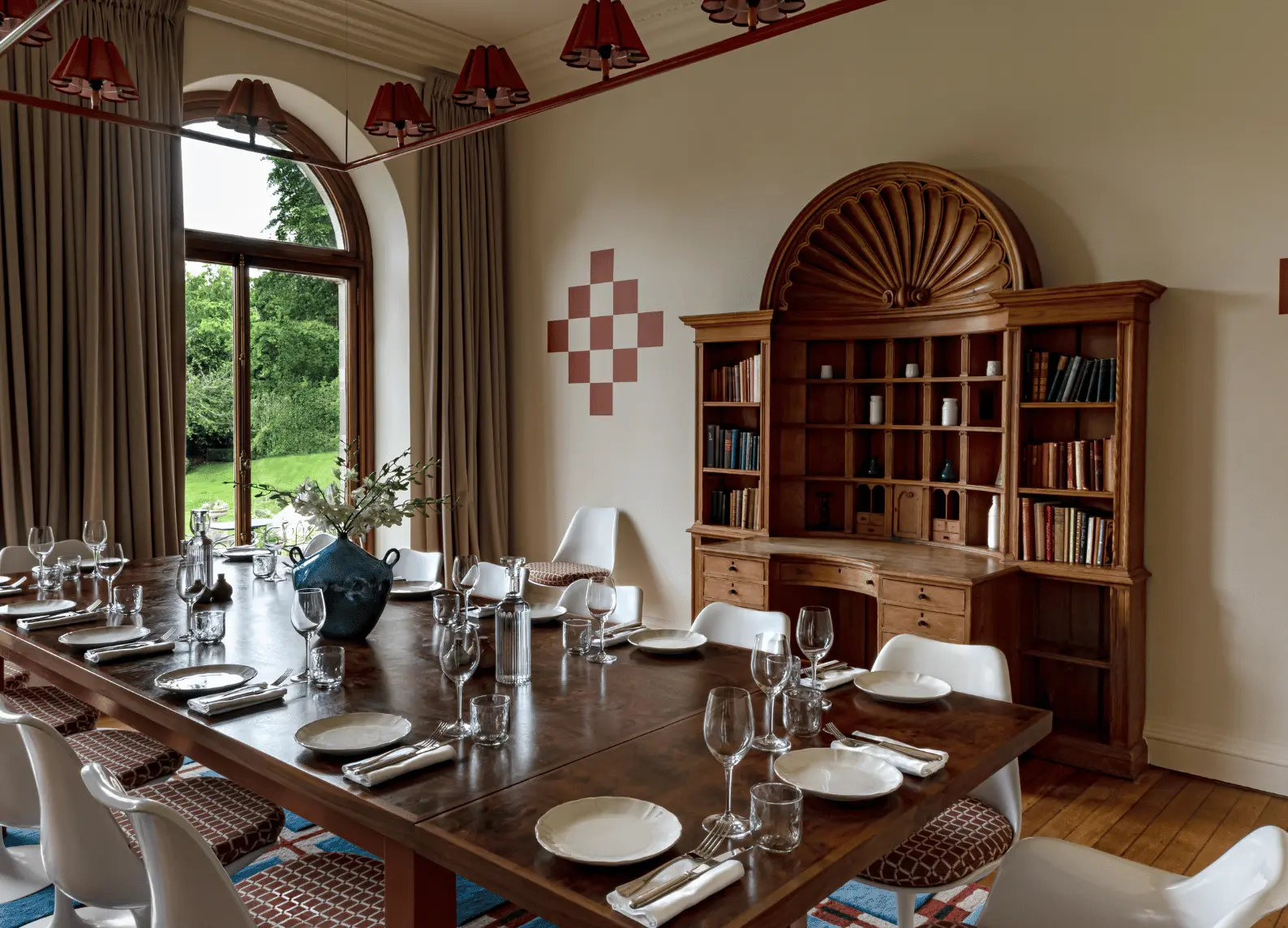 Sala da pranzo privata con grande tavolo in legno, sedie bianche e finestra ad arco affacciata sul giardino, Cowley Manor Experimental, Cotswolds.