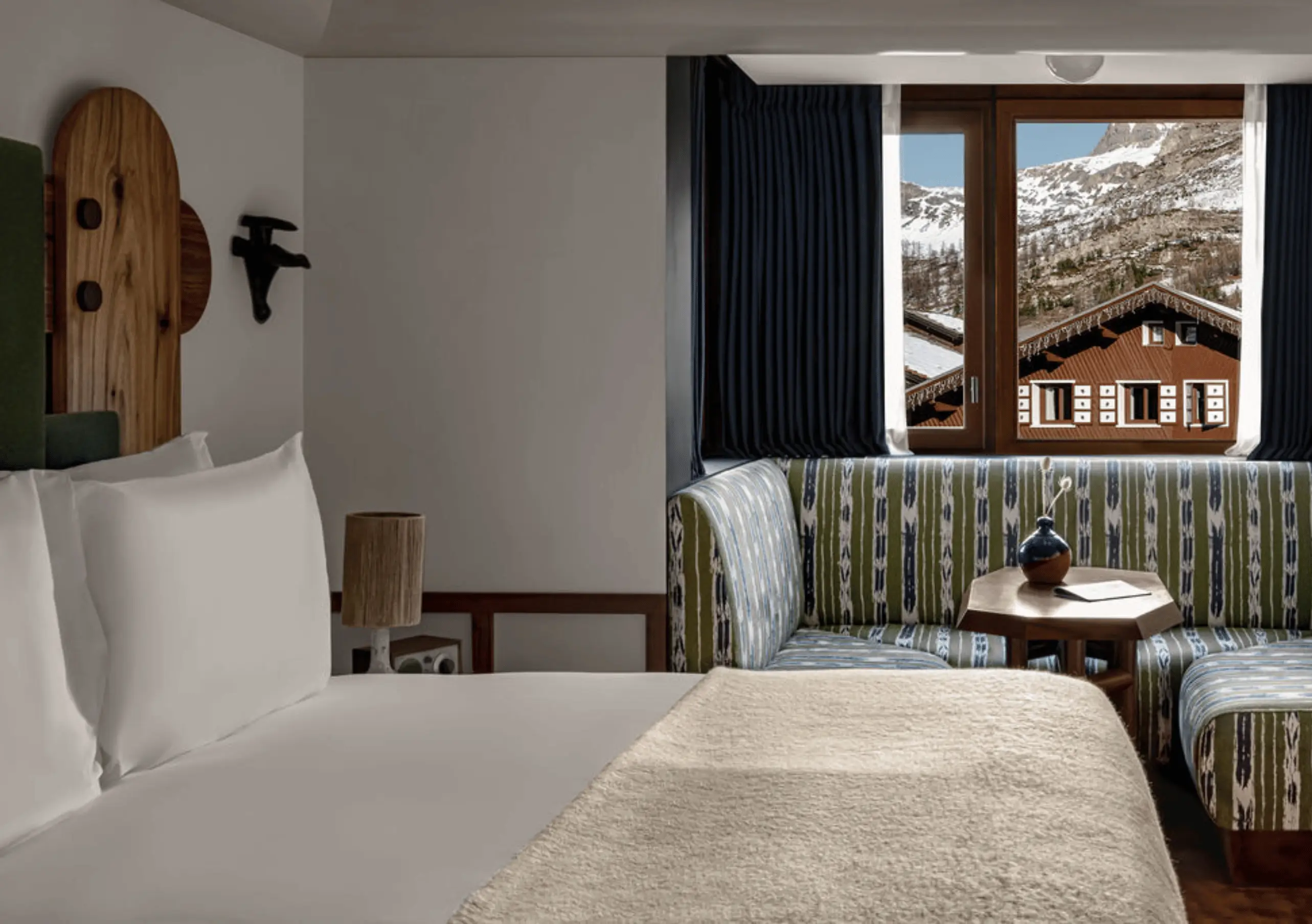 Bedroom with a white double bed, wooden Alpine headboard and a mountain village view through the window in the Val d'Isère Mountain View at Experimental Chalet Val d'Isère