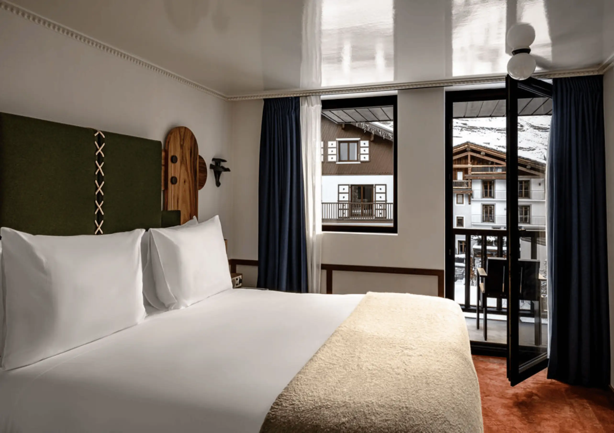 Bedroom with a white double bed, wooden Alpine headboard and navy blue curtains in the Val d'Isère Balcony at Experimental Chalet Val d'Isère