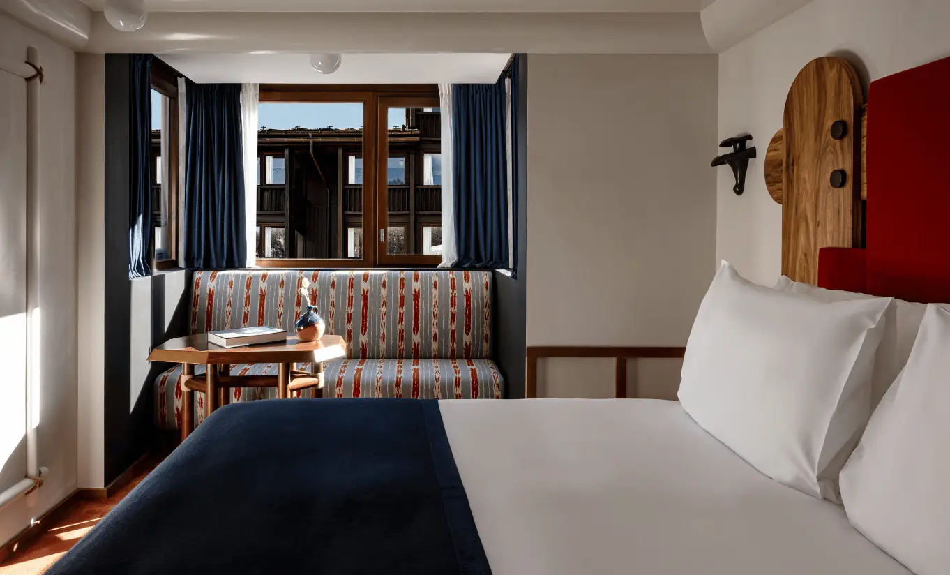 Bedroom with a white double bed, wooden Alpine headboard, navy blue shelving and red accents in the Val d'Isère room at Experimental Chalet Val d'Isère