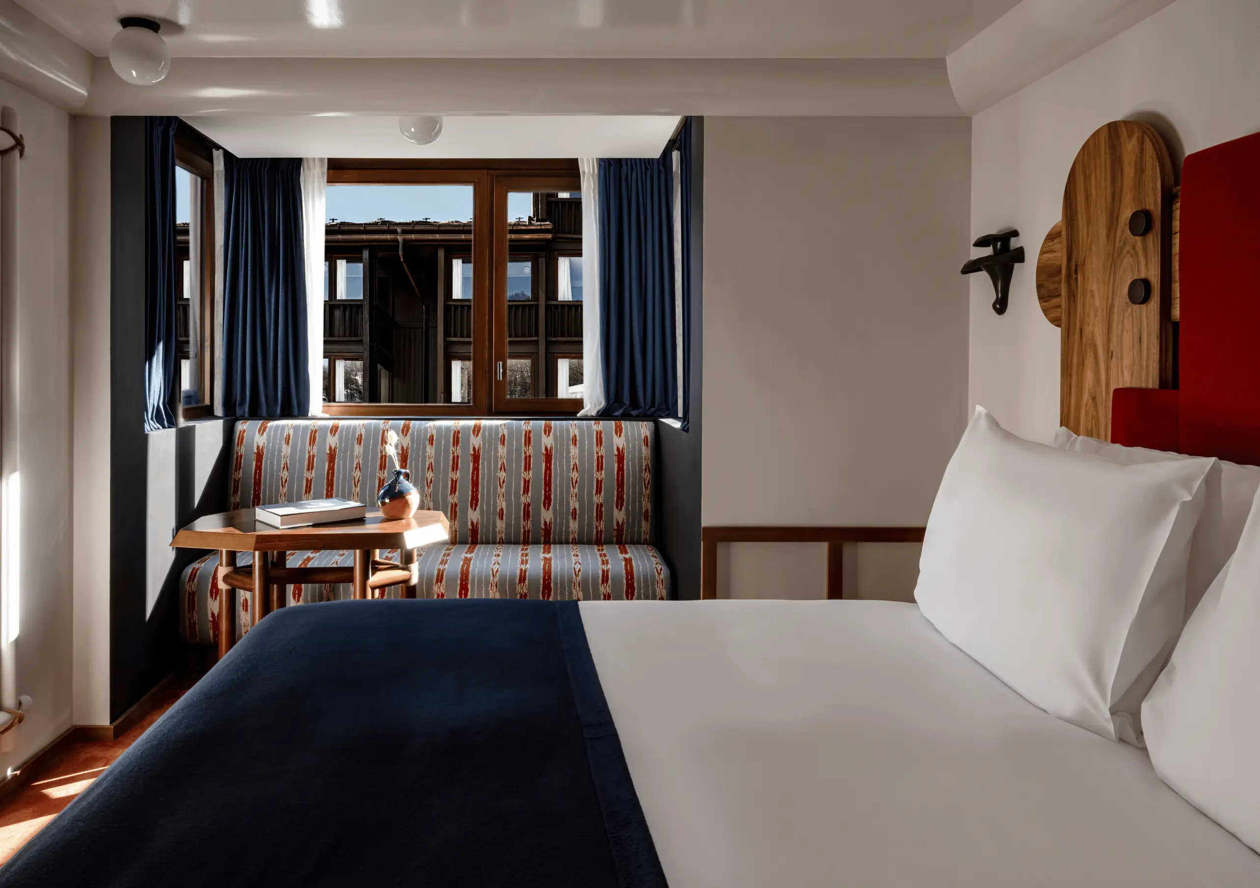 Bedroom with a white double bed, wooden Alpine headboard, navy blue shelving and red accents in the Val d'Isère room at Experimental Chalet Val d'Isère