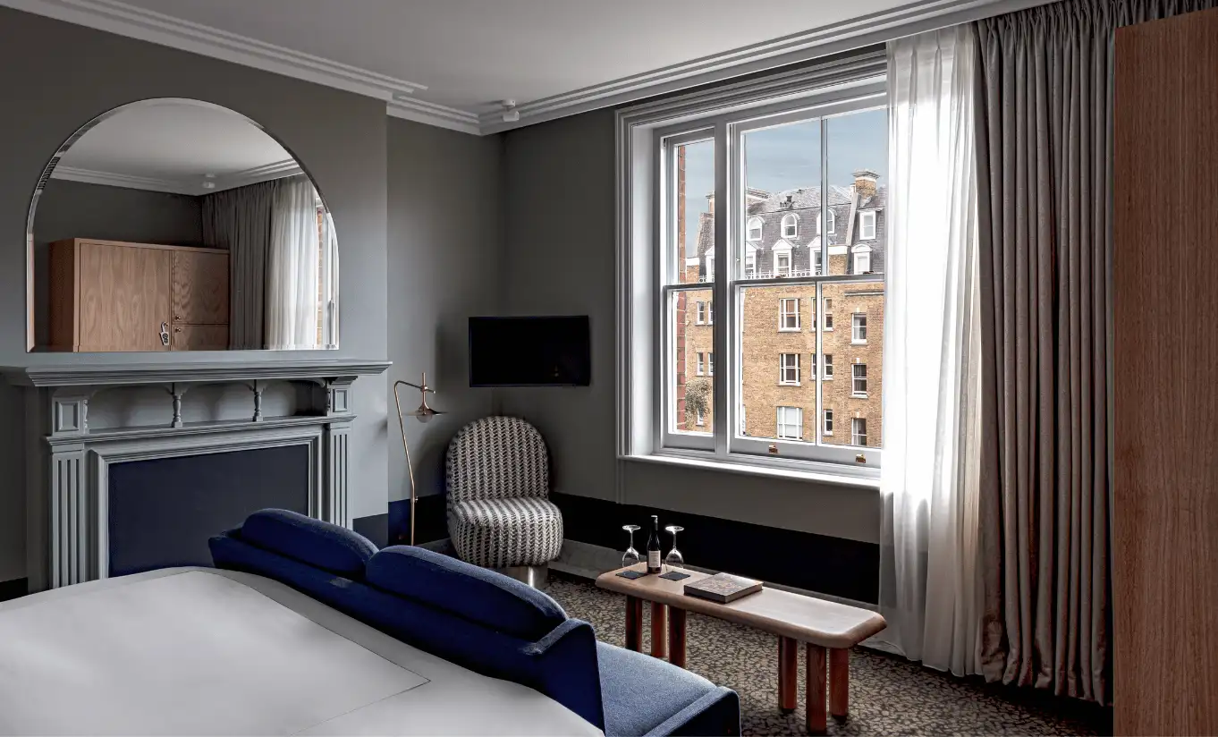 Bedroom with a white double bed, grey walls, a fireplace and linen curtains in the Saint Paul Executive Room at Henrietta Experimental, boutique hotel in Covent Garden, central London