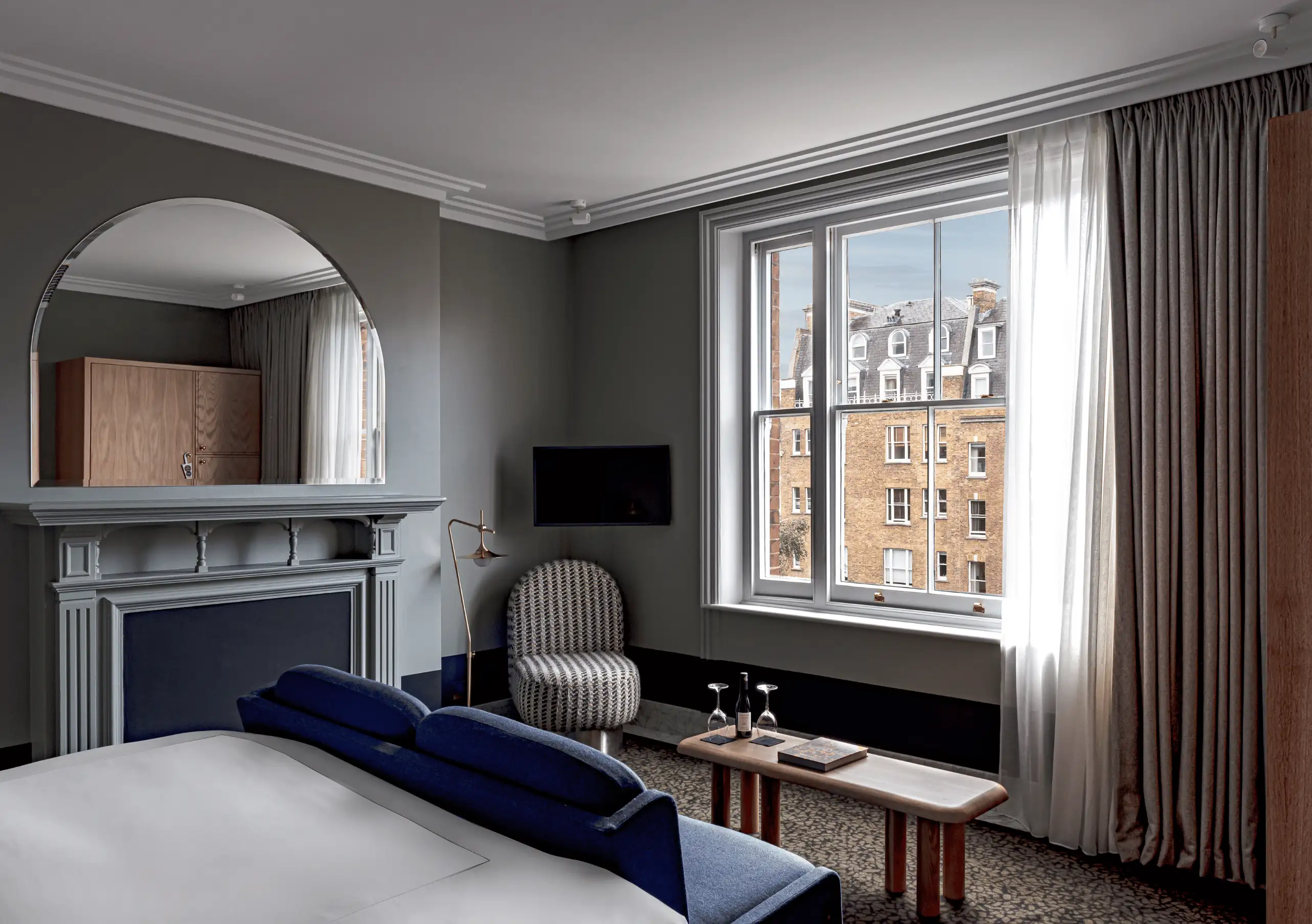 Experimental Group elegant hotel room with grey stone fireplace, cobalt blue velvet chair and large window with Parisian rooftop views.