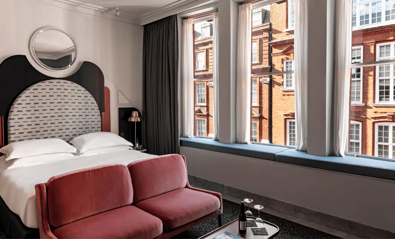Bedroom with a white double bed, a rounded black headboard and large windows overlooking the street in the Henrietta Executive Room at Henrietta Experimental, boutique hotel in central London