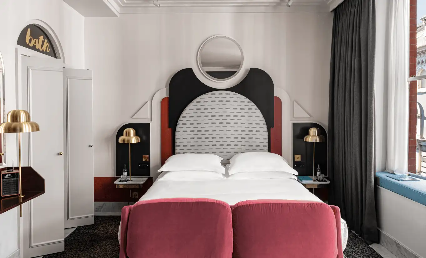 Detail of a white double bed with a curved black headboard, pink velvet cushions and a globe pendant light in the Henrietta Executive Room at Henrietta Experimental, Covent Garden