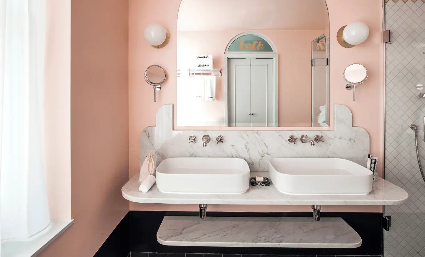 Bright bathroom with pink walls, a double white sink and a large arched mirror in the Henrietta Executive Room at Henrietta Experimental, luxury boutique hotel in central London