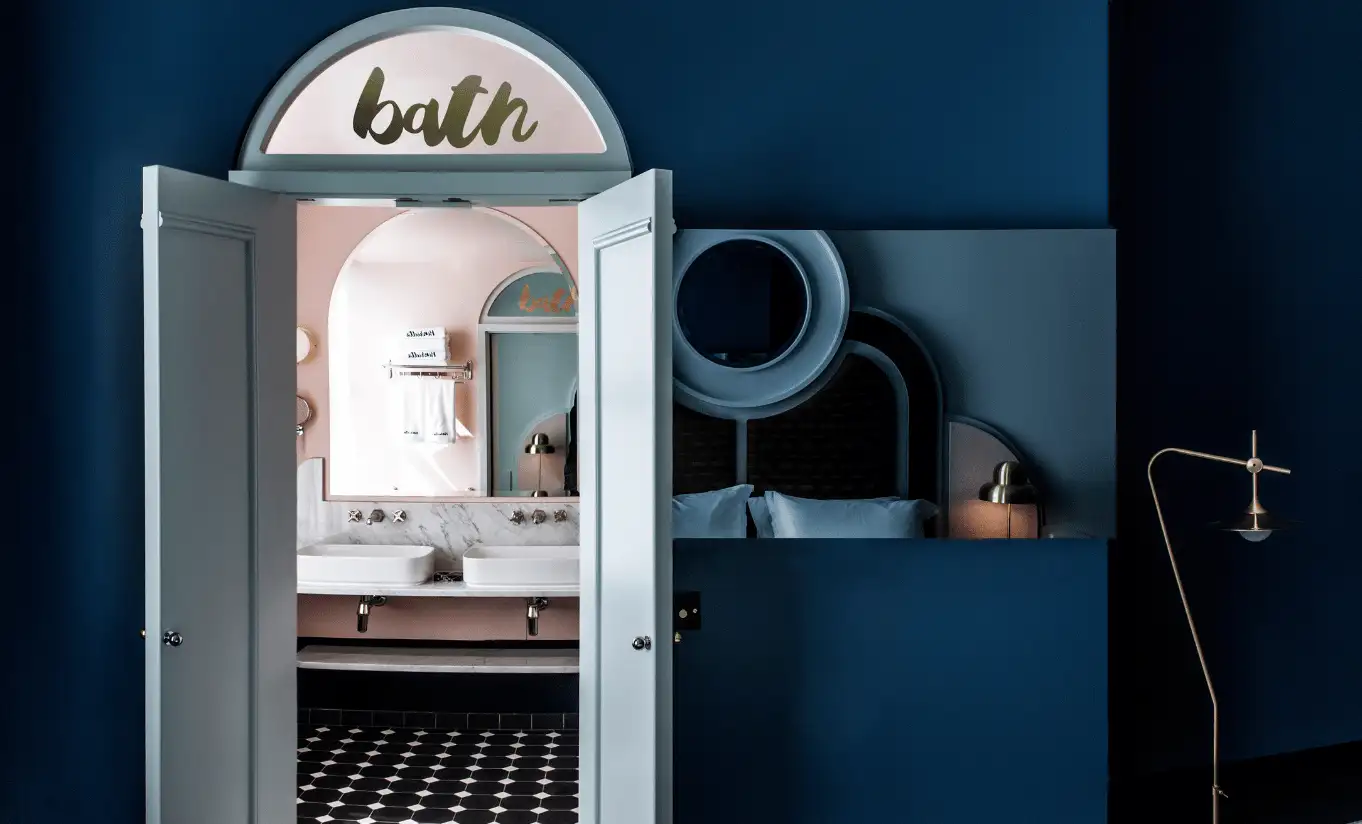 Bathroom entrance with a navy blue door, an arched "bath" sign and a freestanding bathtub in the Henrietta Executive Room at Henrietta Experimental, boutique hotel in Covent Garden