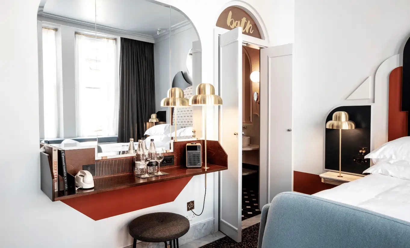 Bedroom with a white double bed, a red carpet, an arched mirror and gold lighting in the Henrietta Executive Room at Henrietta Experimental, boutique hotel in Covent Garden, central London