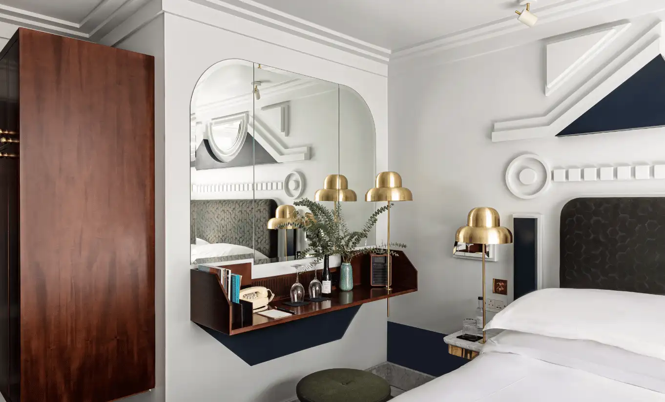Bedroom with a white double bed, a wooden wardrobe, gold lighting and an arched mirror in the London Eye Superior Terrace room at Henrietta Experimental, Covent Garden