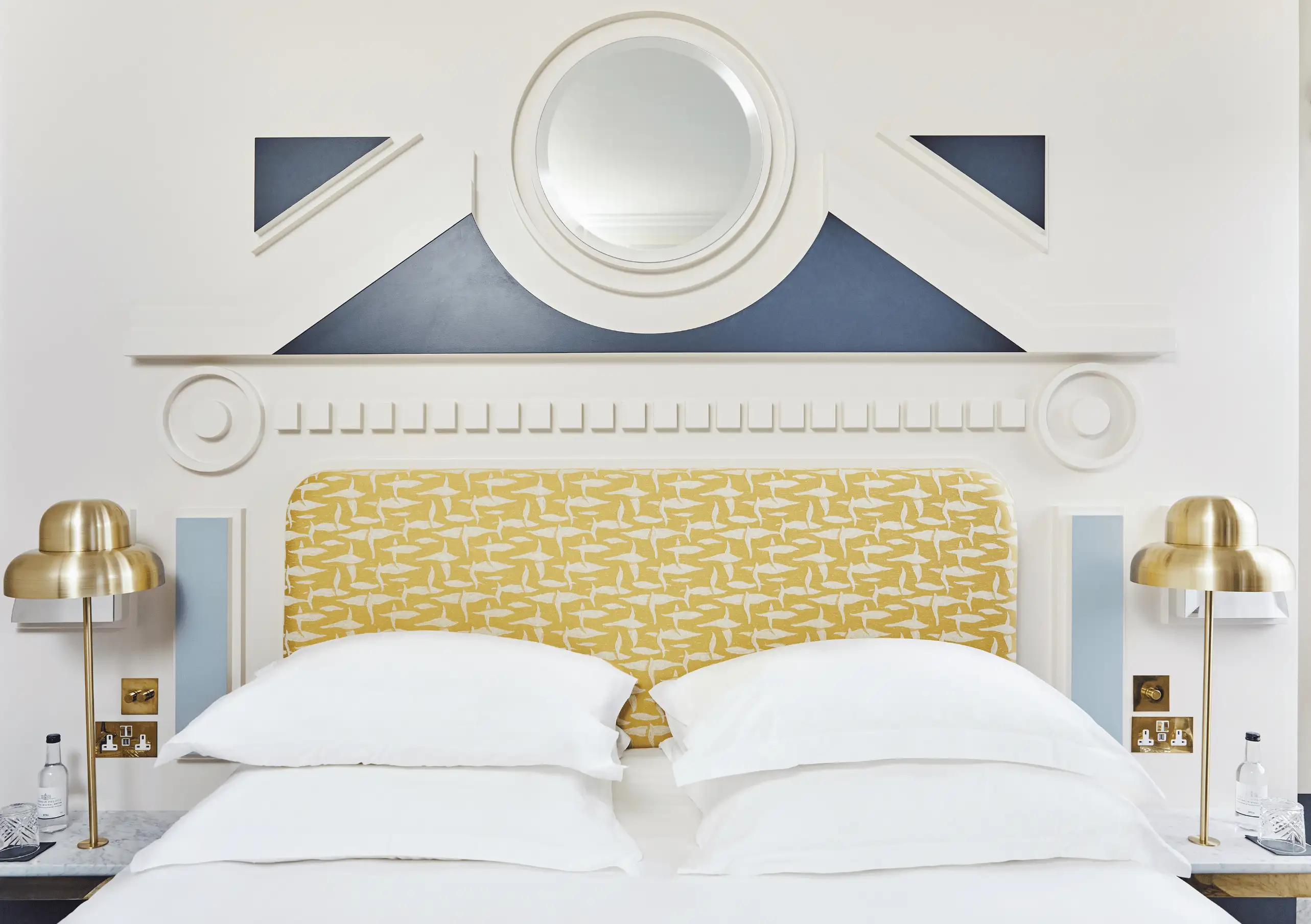 Experimental Group luxury hotel bedroom featuring a golden quilted headboard, white bedding and nautical navy stripe wall decor.