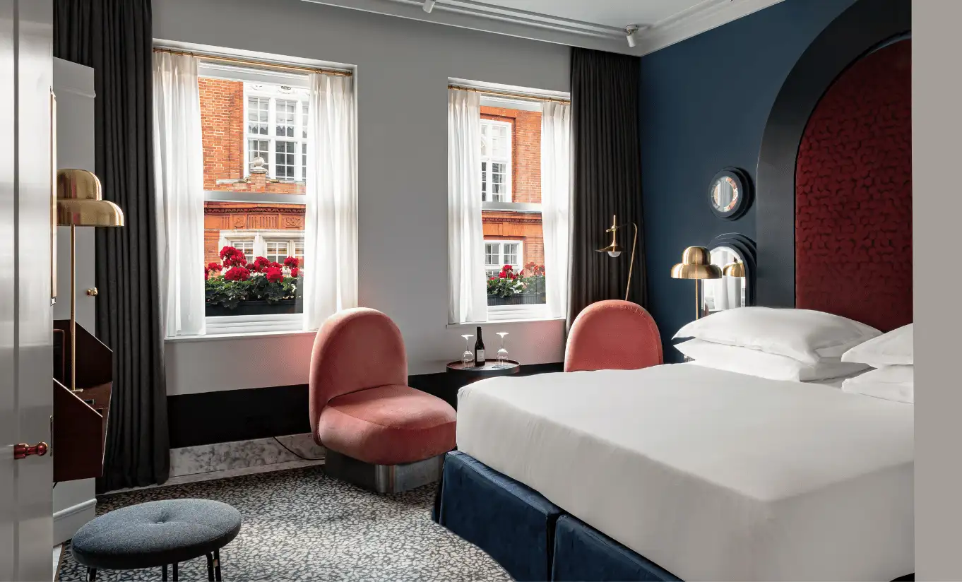 Bedroom with a white double bed, navy blue walls, pink velvet armchairs and large windows in the Covent Garden Superior Room at Henrietta Experimental, boutique hotel in central London
