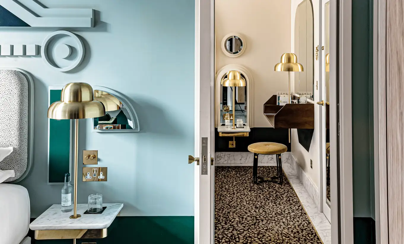Corridor with teal blue walls, gold lighting and a patterned floor leading to the room in the Floral Superior Room at Henrietta Experimental, luxury boutique hotel in central London