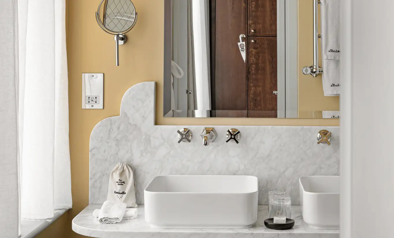 Bathroom with a white pedestal sink, ornate gold taps and a round mirror in the Floral Superior Room at Henrietta Experimental, boutique hotel in Covent Garden