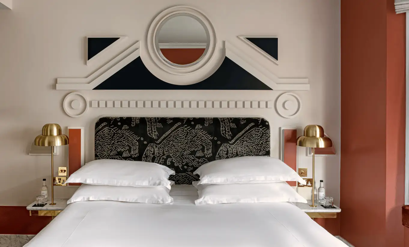 Bedroom with a white double bed, a dark patterned headboard, gold wall lights and terracotta walls in the Floral Superior Room at Henrietta Experimental, Covent Garden