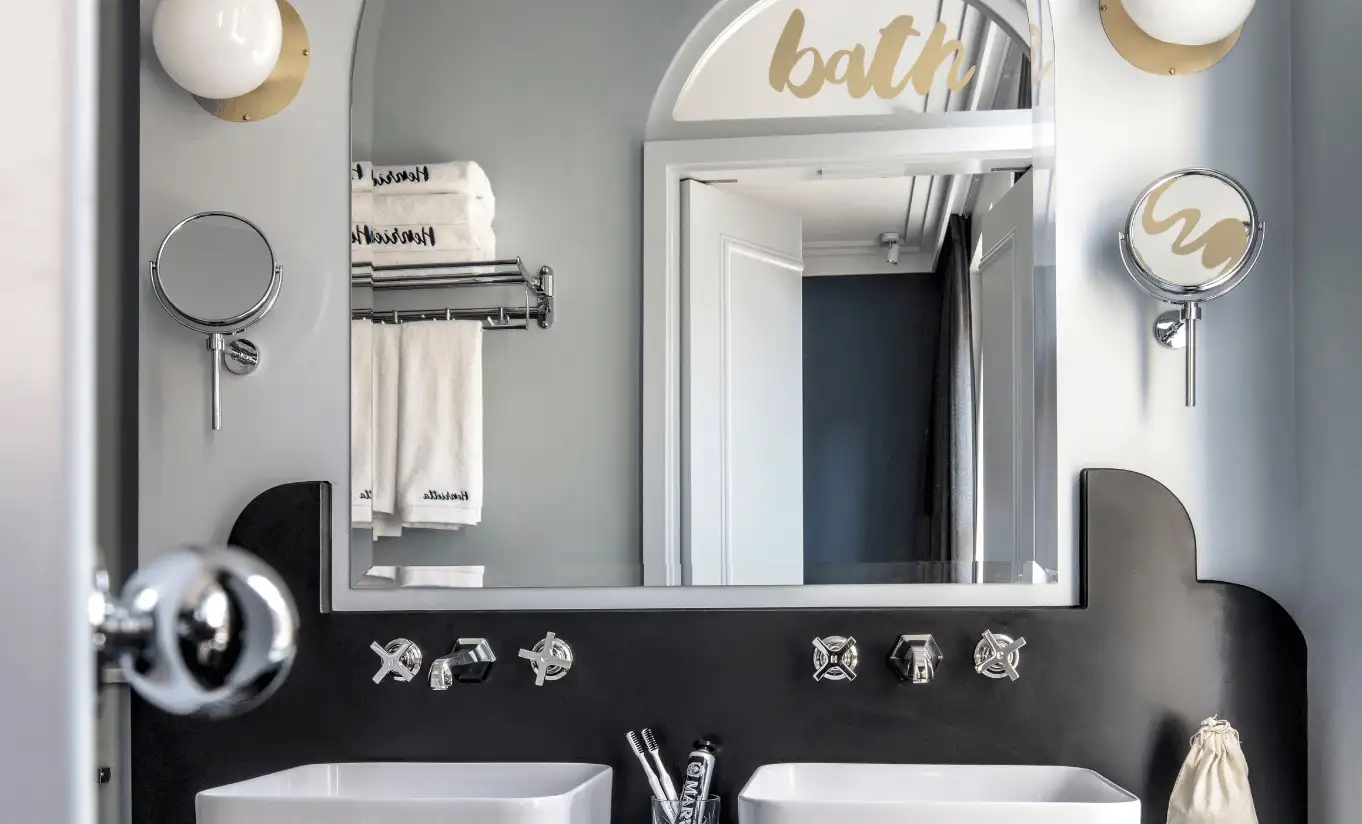 Bathroom with a black sink, vintage brass taps, a round mirror and a "bath" sign on the wall in the Covent Garden Superior Room at Henrietta Experimental, luxury boutique hotel in central London