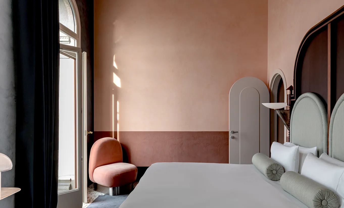 Il Palazzo Experimental hotel room with dusty pink walls, velvet terracotta chair and arched door detail in Venice