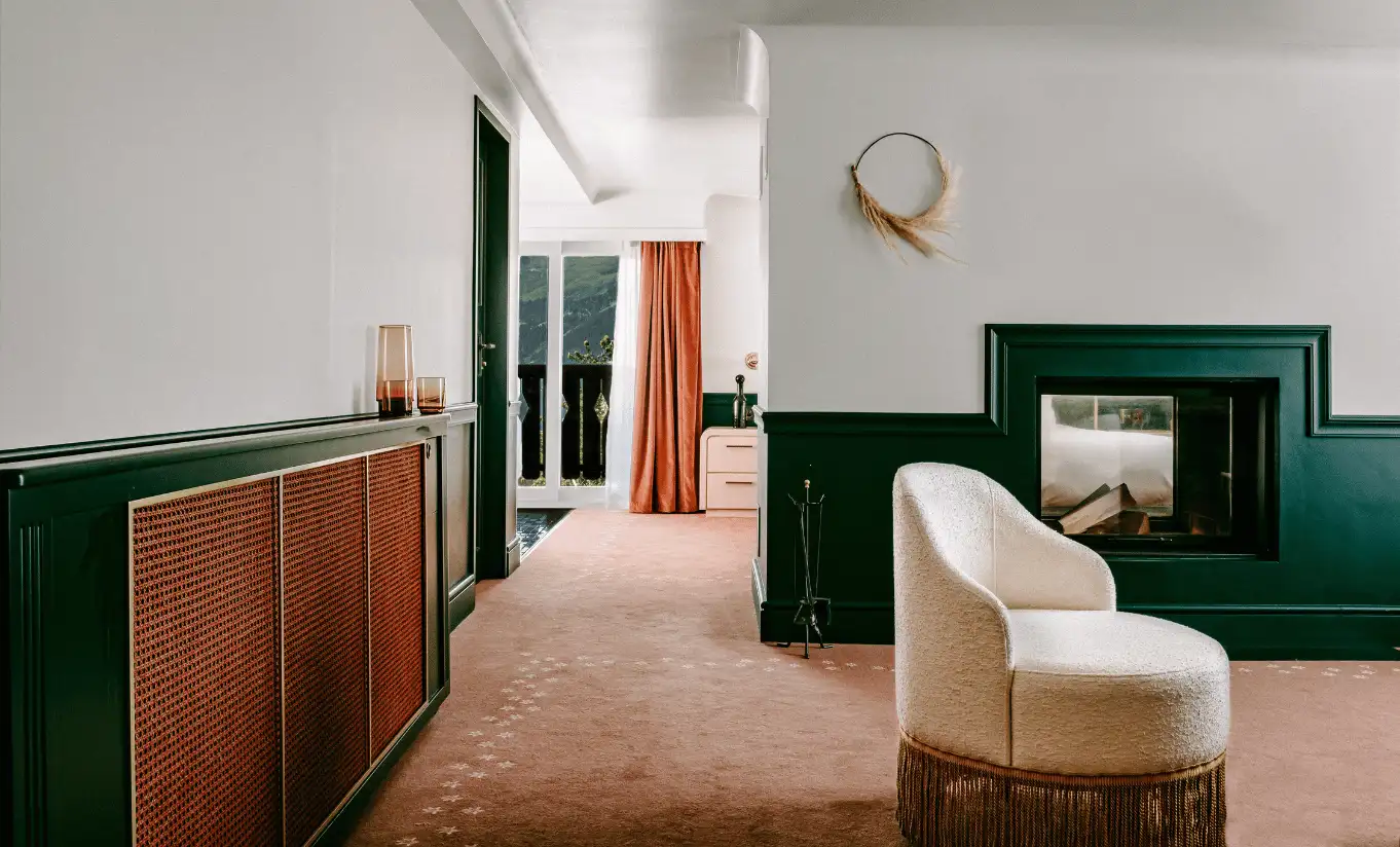 Bright living area with a white armchair, dark green fireplace surround and warm carpet in the Panorama Suite at Experimental Chalet Verbier