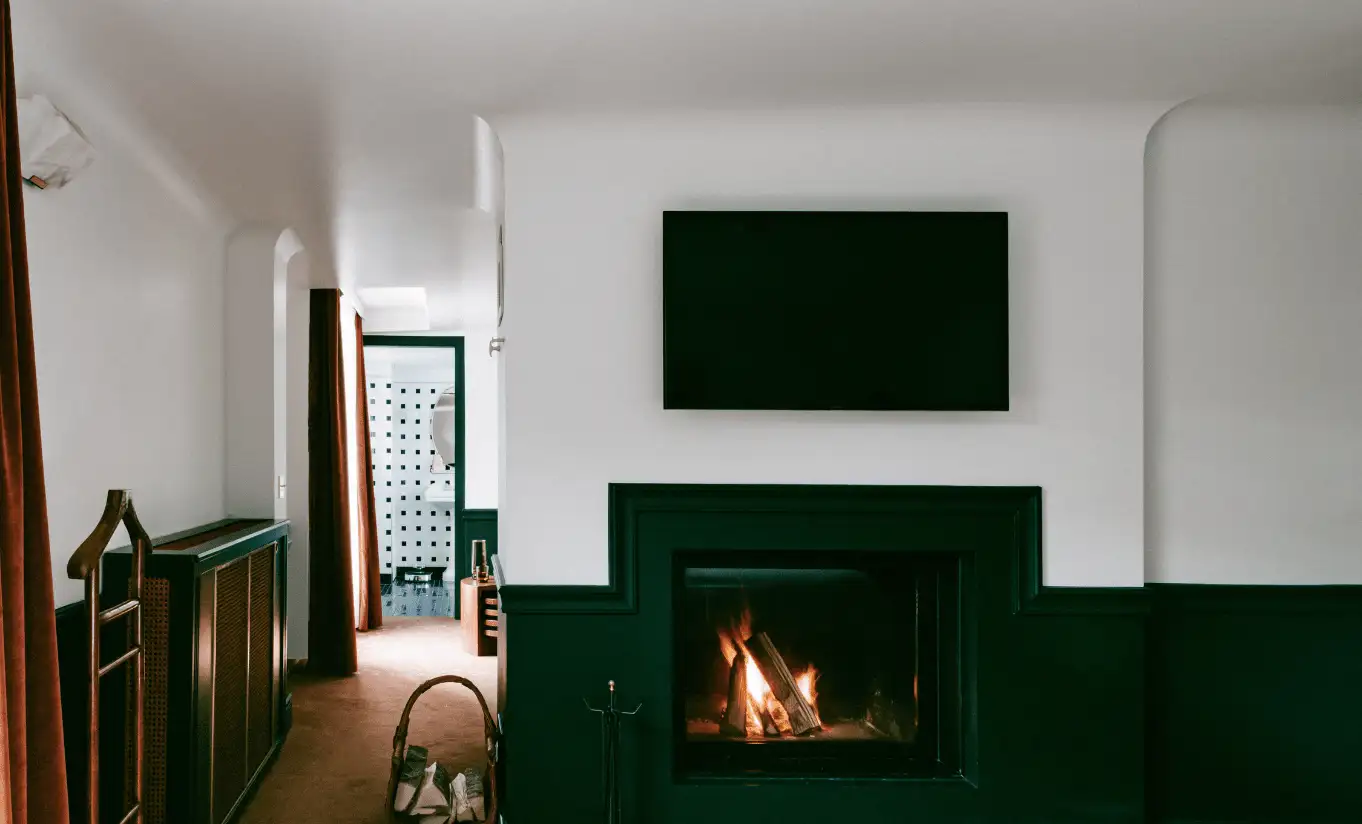 Cosy living area with a lit fireplace and dark green surround in the Verbier Suite at Experimental Chalet Verbier