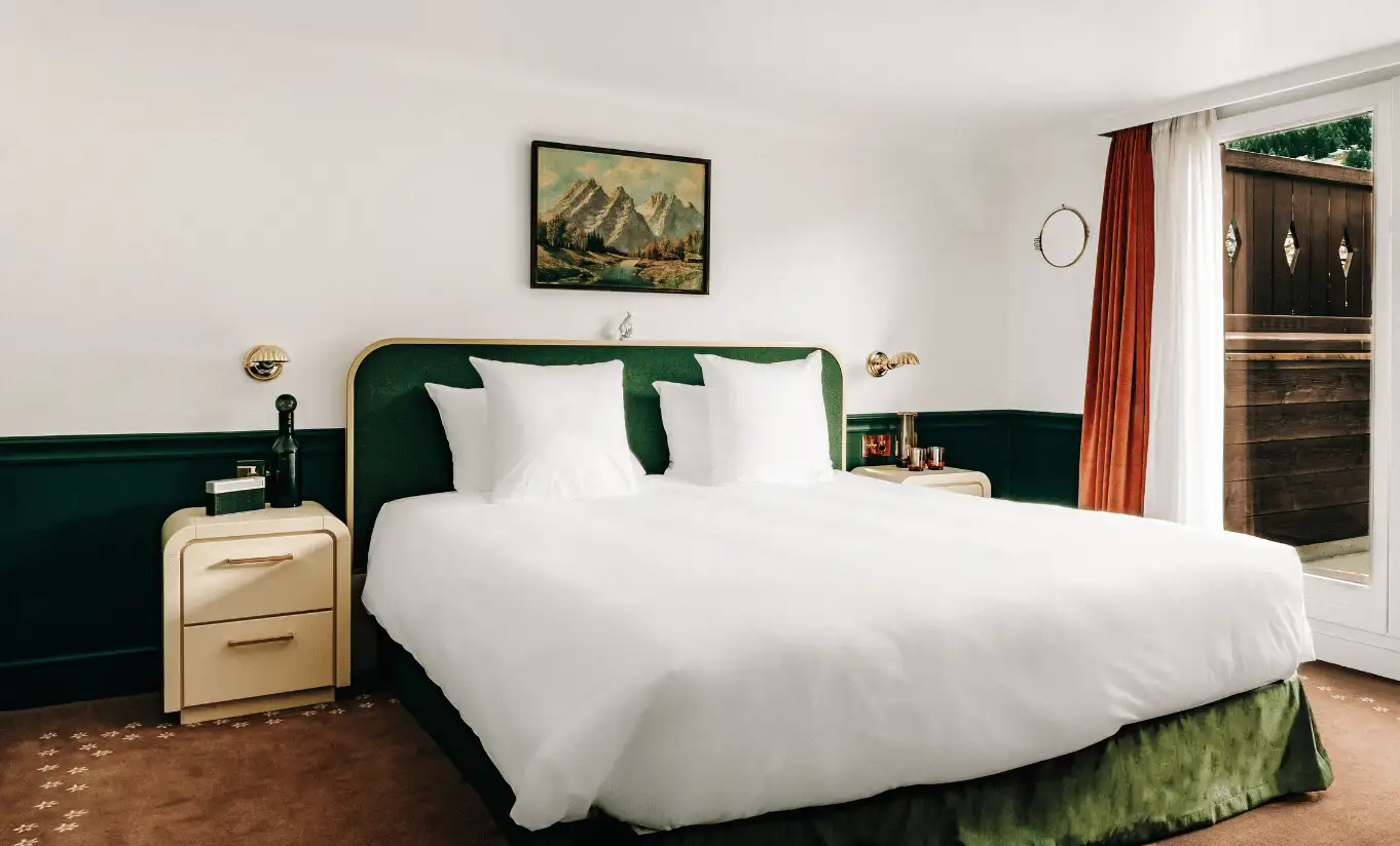 Bright bedroom with a white double bed, green headboard and red curtains in the Verbier Suite at Experimental Chalet Verbier