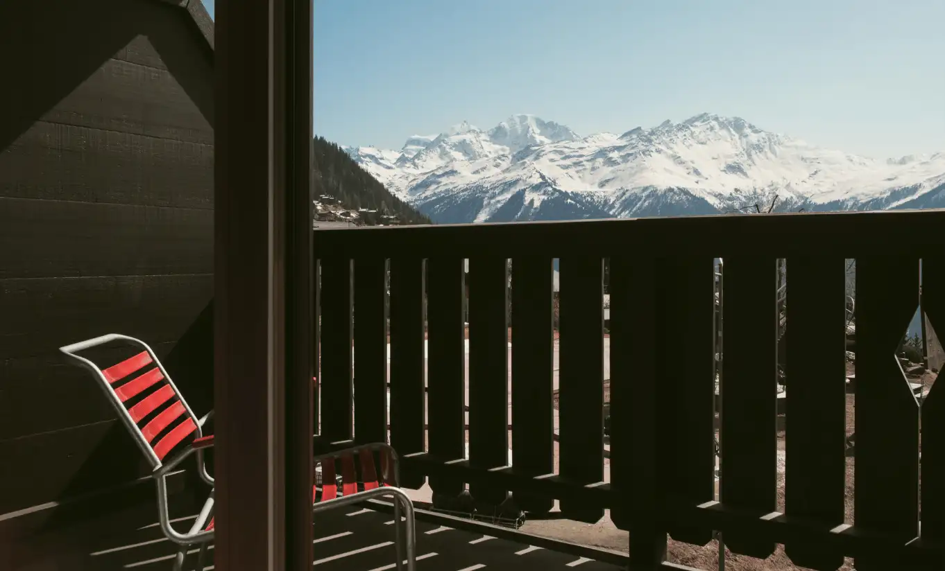 Private terrace with a red deck chair and a panoramic view of the snowy Swiss Alps in the Superior Room Terrace at Experimental Chalet Verbier