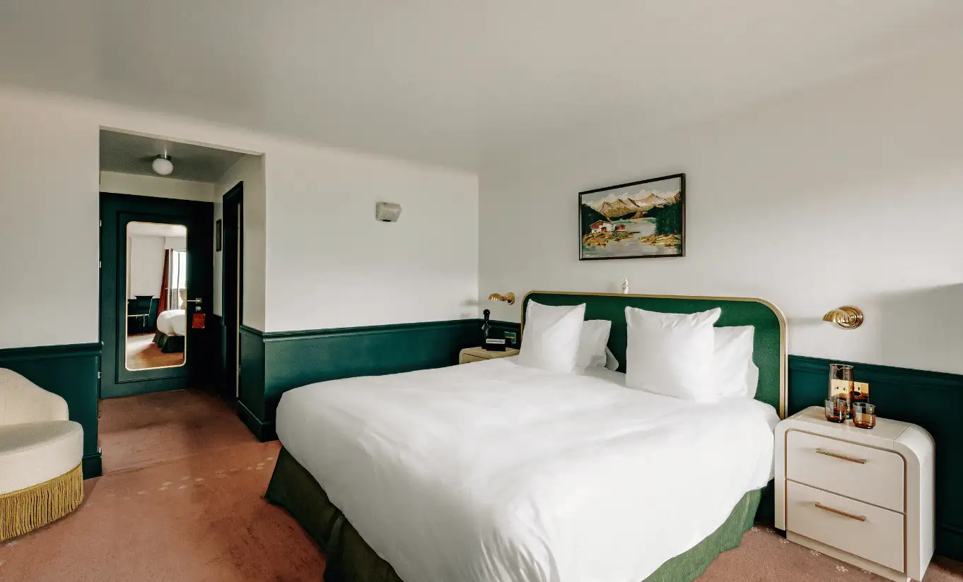 Bright bedroom with a white double bed and dark green wainscoting in the Superior Room at Experimental Chalet Verbier