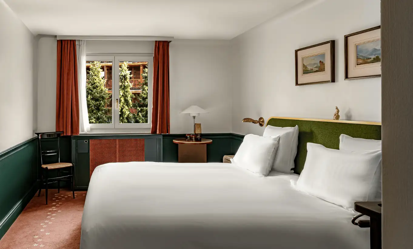 Bright bedroom with a white double bed, olive green headboard, red curtains and a window in the Classic Room at Experimental Chalet Verbier