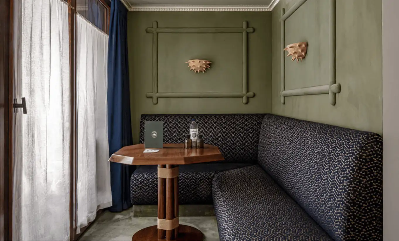 Coin salon intime avec canapé à motifs, table ronde et murs vert sauge dans la Junior Suite Solaise de l'Experimental Chalet Val d'Isère