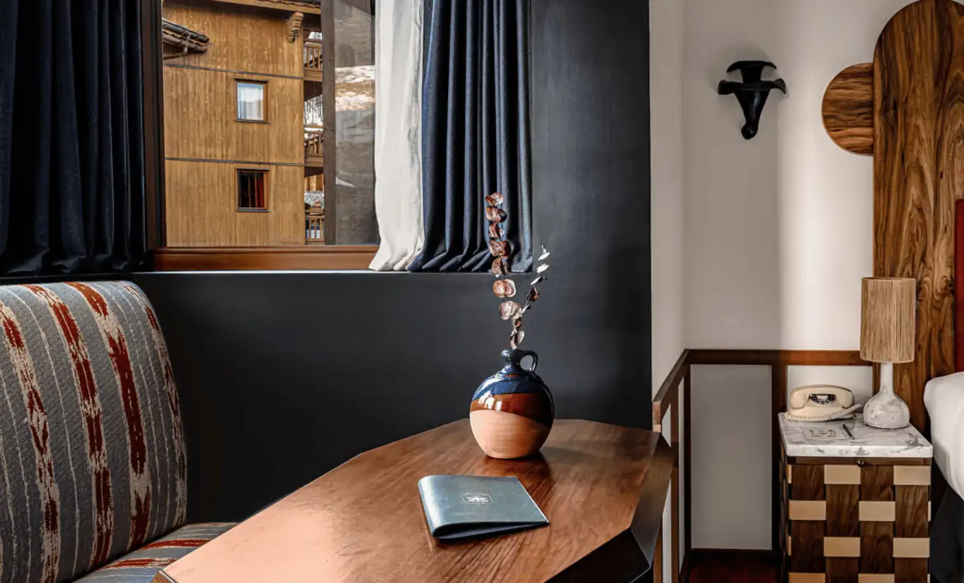 Coin salon aux tons sombres avec fauteuil à motifs, table de nuit en bois et œuvre alpine dans l'Olympique Deluxe de l'Experimental Chalet Val d'Isère