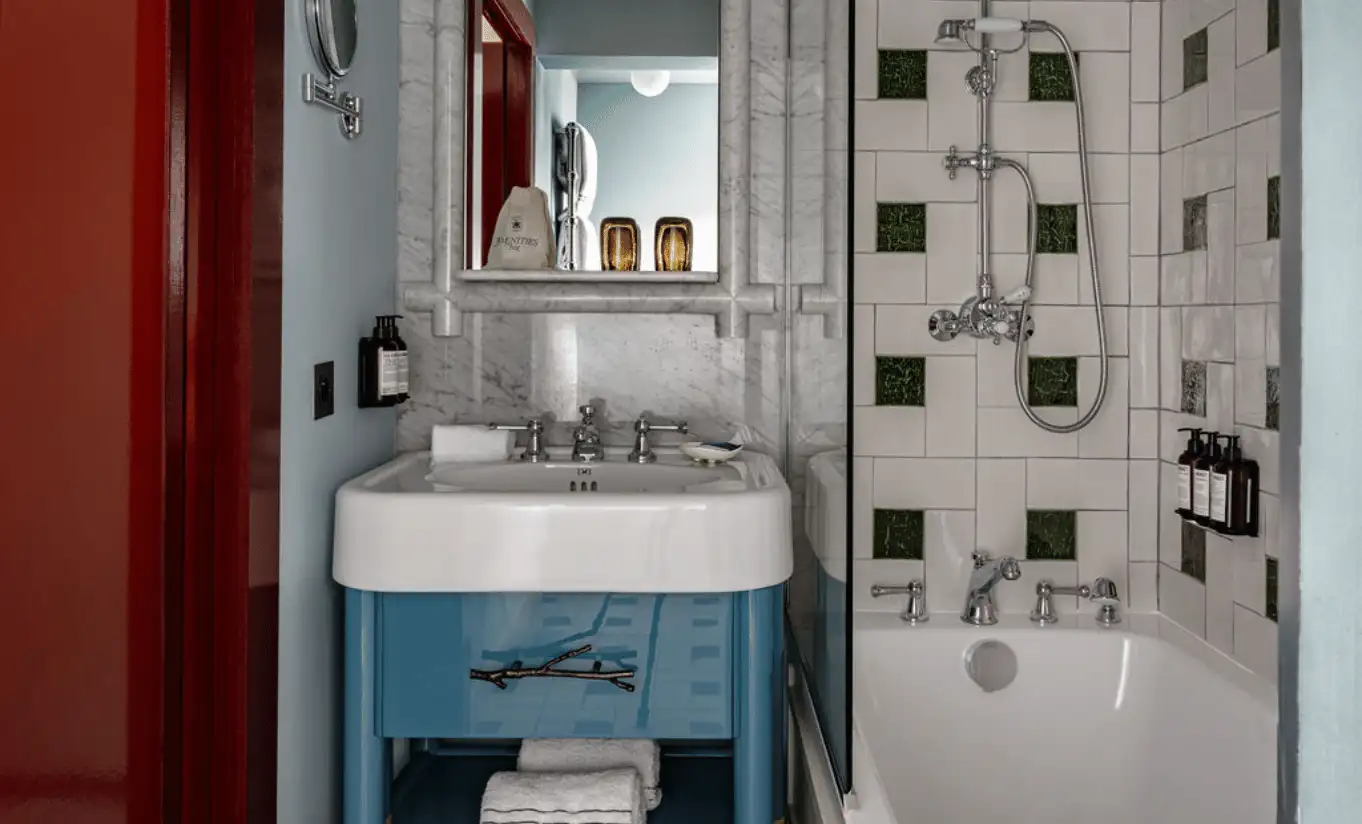 Compact bathroom with dark geometric tiles, a blue basin and a walk-in shower in the Val d'Isère Under the Eaves at Experimental Chalet Val d'Isère