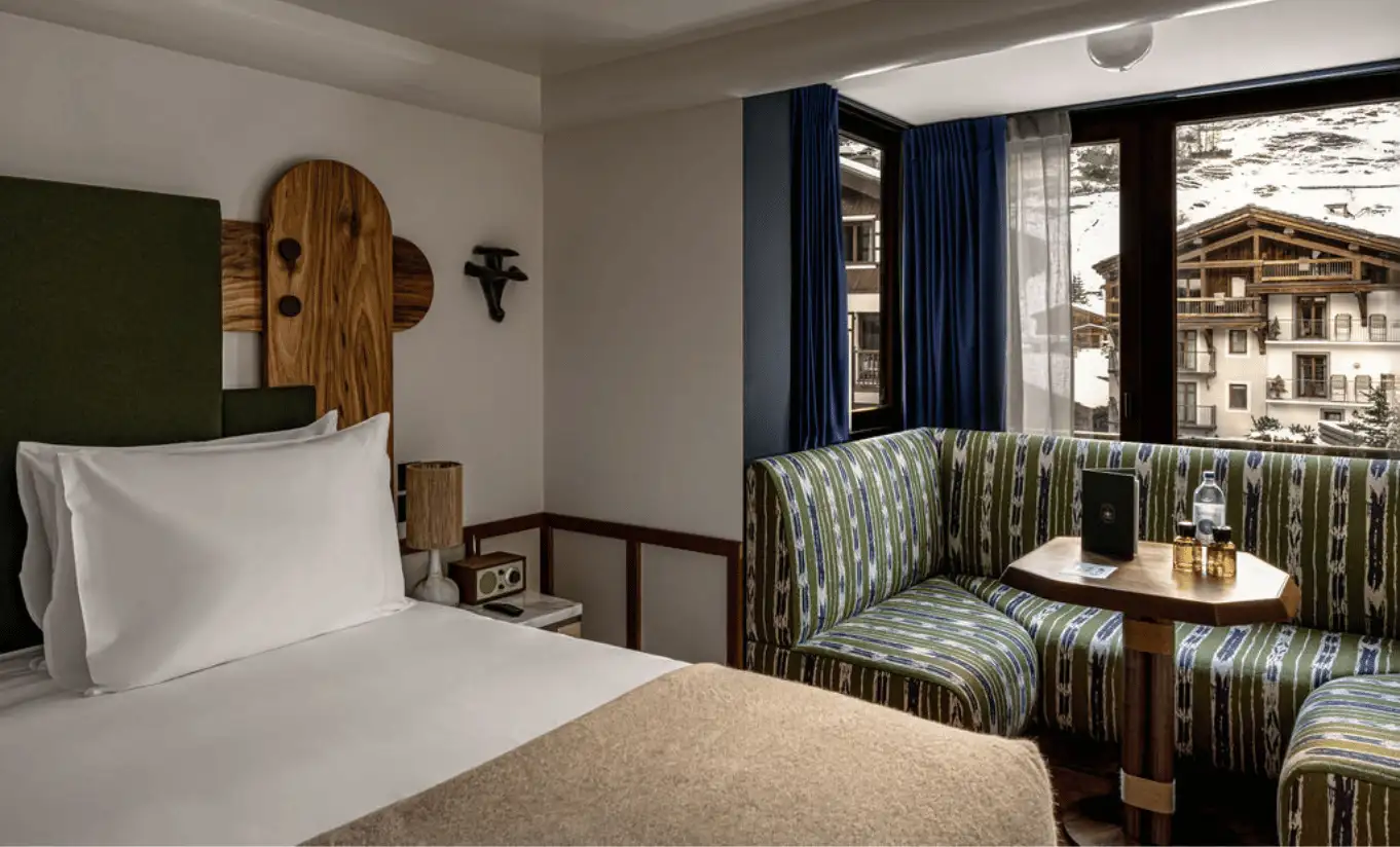 Bright bedroom with a white double bed, wooden Alpine headboard and navy blue curtains in the Val d'Isère Mountain View at Experimental Chalet Val d'Isère