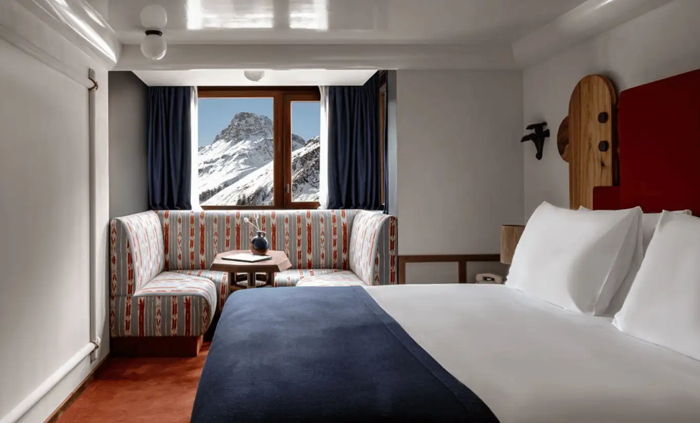 Bedroom with a white double bed, red sofa and a snowy mountain view through the window in the Val d'Isère Mountain View at Experimental Chalet Val d'Isère