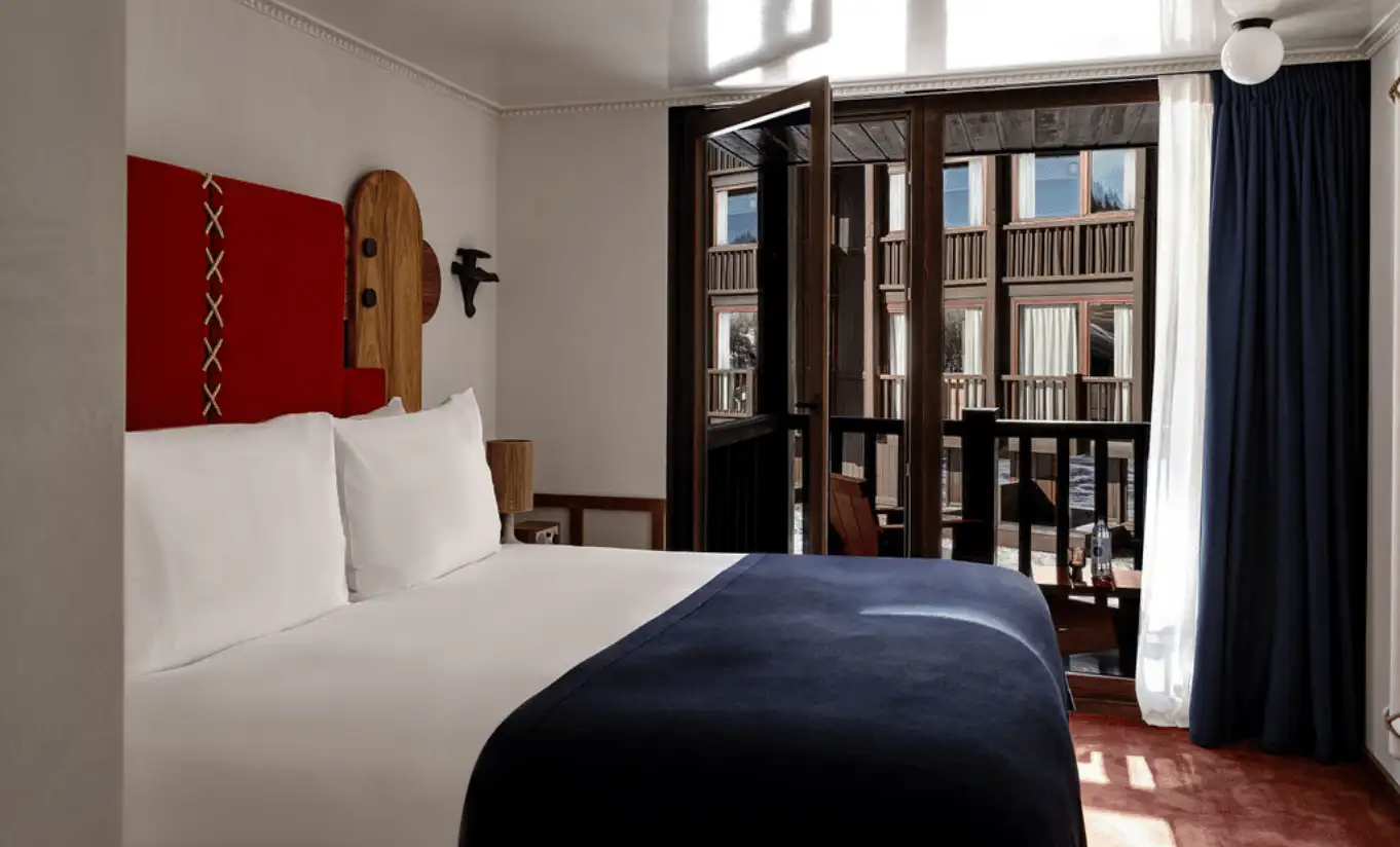 Bedroom with a white double bed, red wall accents and black French doors in the Val d'Isère Balcony at Experimental Chalet Val d'Isère