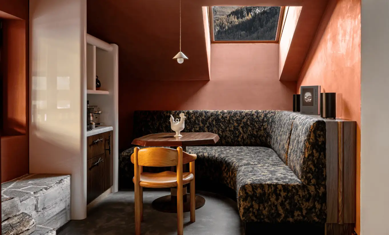 Attic sitting area with terracotta walls, a patterned sofa and wooden furniture in the Iseran Suite at Experimental Chalet Val d'Isère