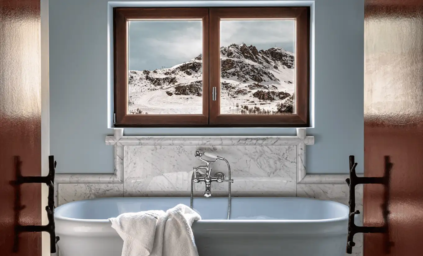  Blue-toned bathroom with a freestanding bathtub and a snowy mountain view through the window in the Bellevarde Suite at Experimental Chalet Val d'Isère