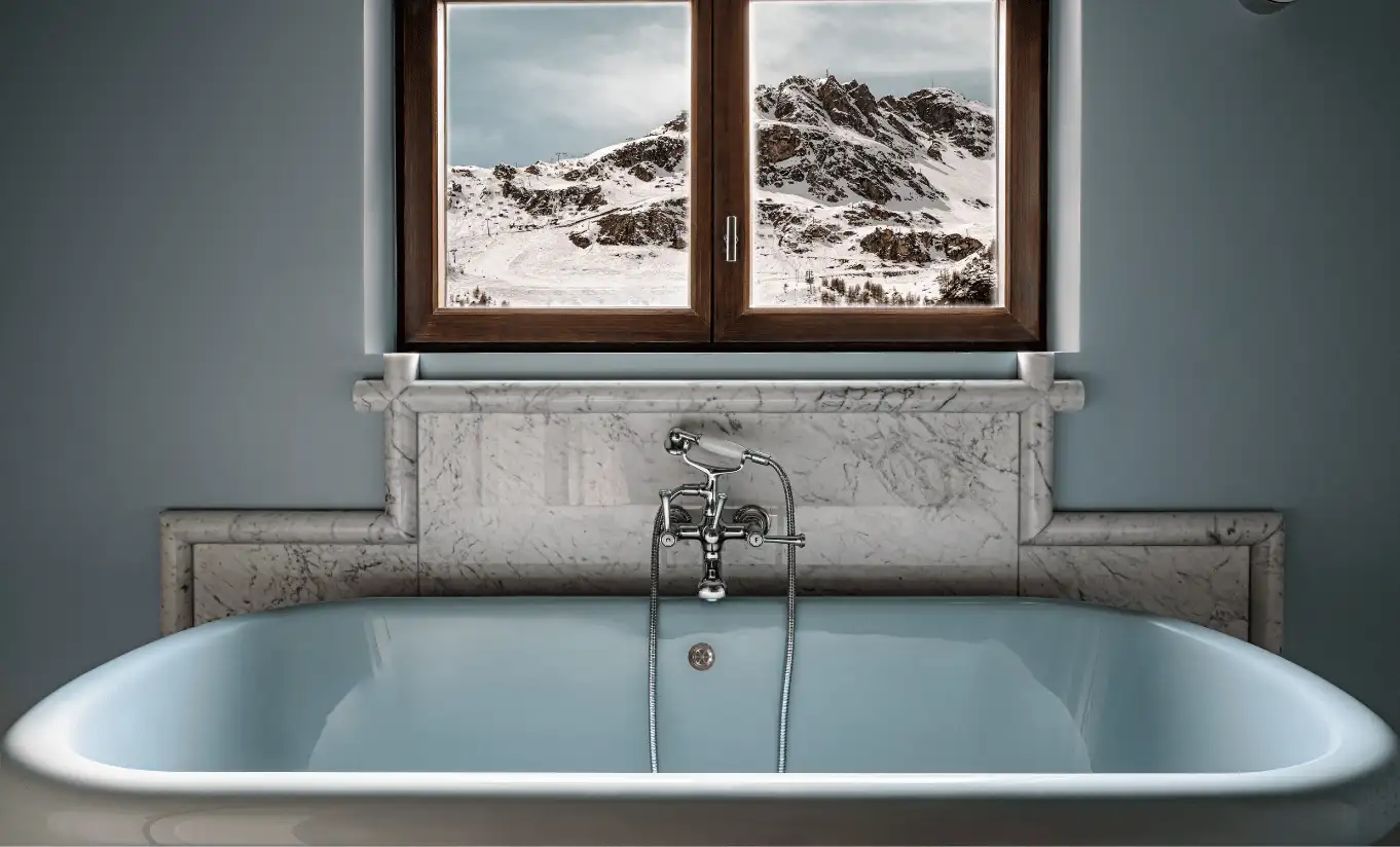Close-up of a freestanding bathtub with a snowy mountain view through the window in the Bellevarde Suite at Experimental Chalet Val d'Isère